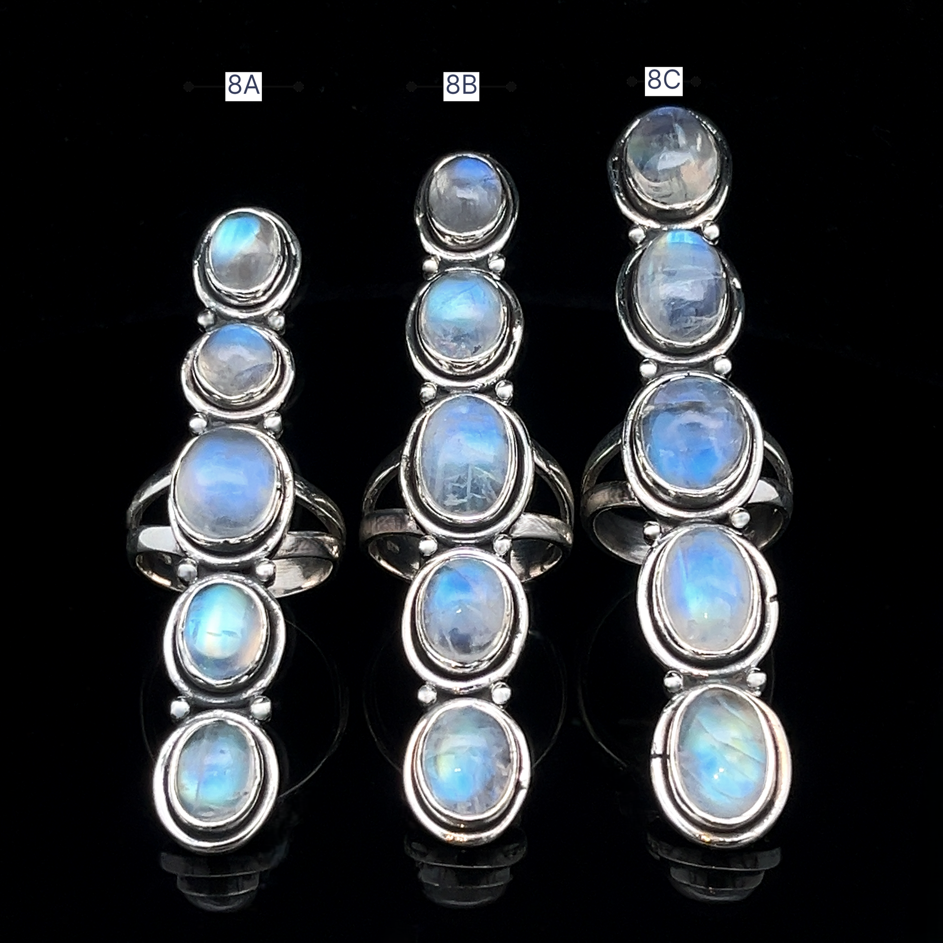 Three Moonstone Ladder Rings in sterling silver, each set with five oval iridescent moonstones, are displayed upright against a black background.