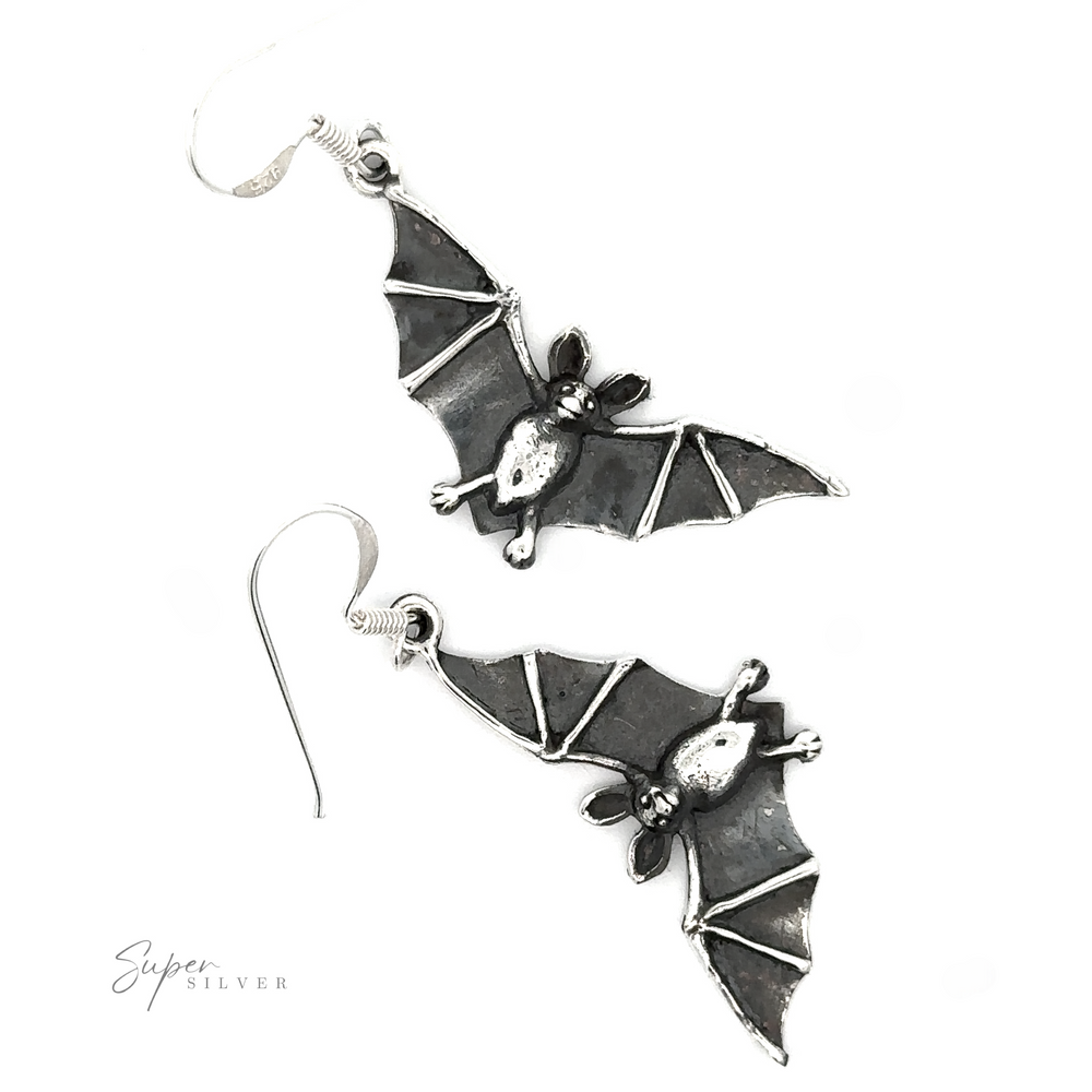 
                  
                    A pair of Flying Bat Earrings with a Gothic aesthetic and intricate details, displayed on a white background with a signature at the bottom right.
                  
                