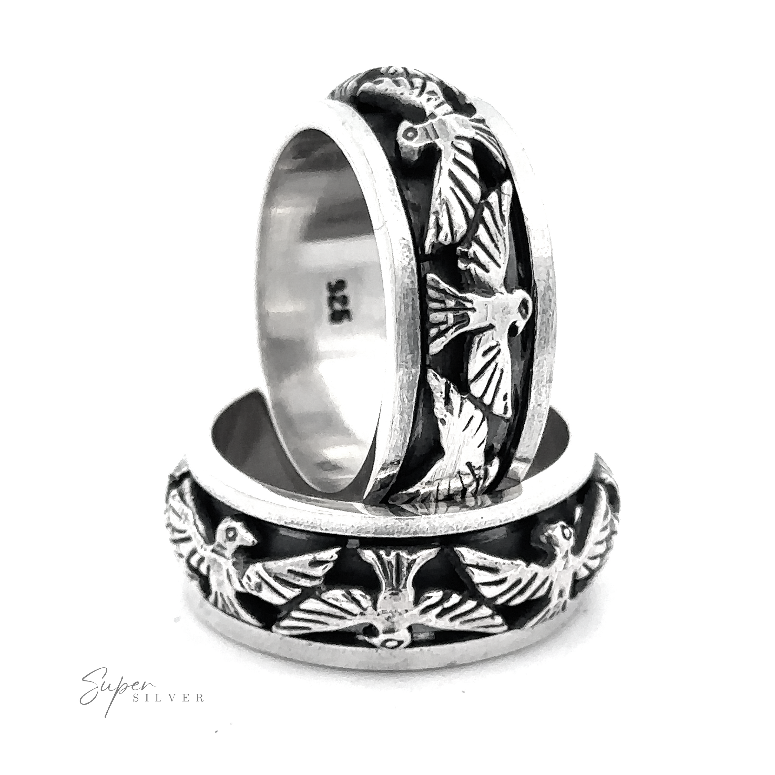 Two silver rings with intricate thunderbird engravings on the bands are stacked against a white background. The words "Thick Thunderbird Spinner Ring" appear in the lower left corner.