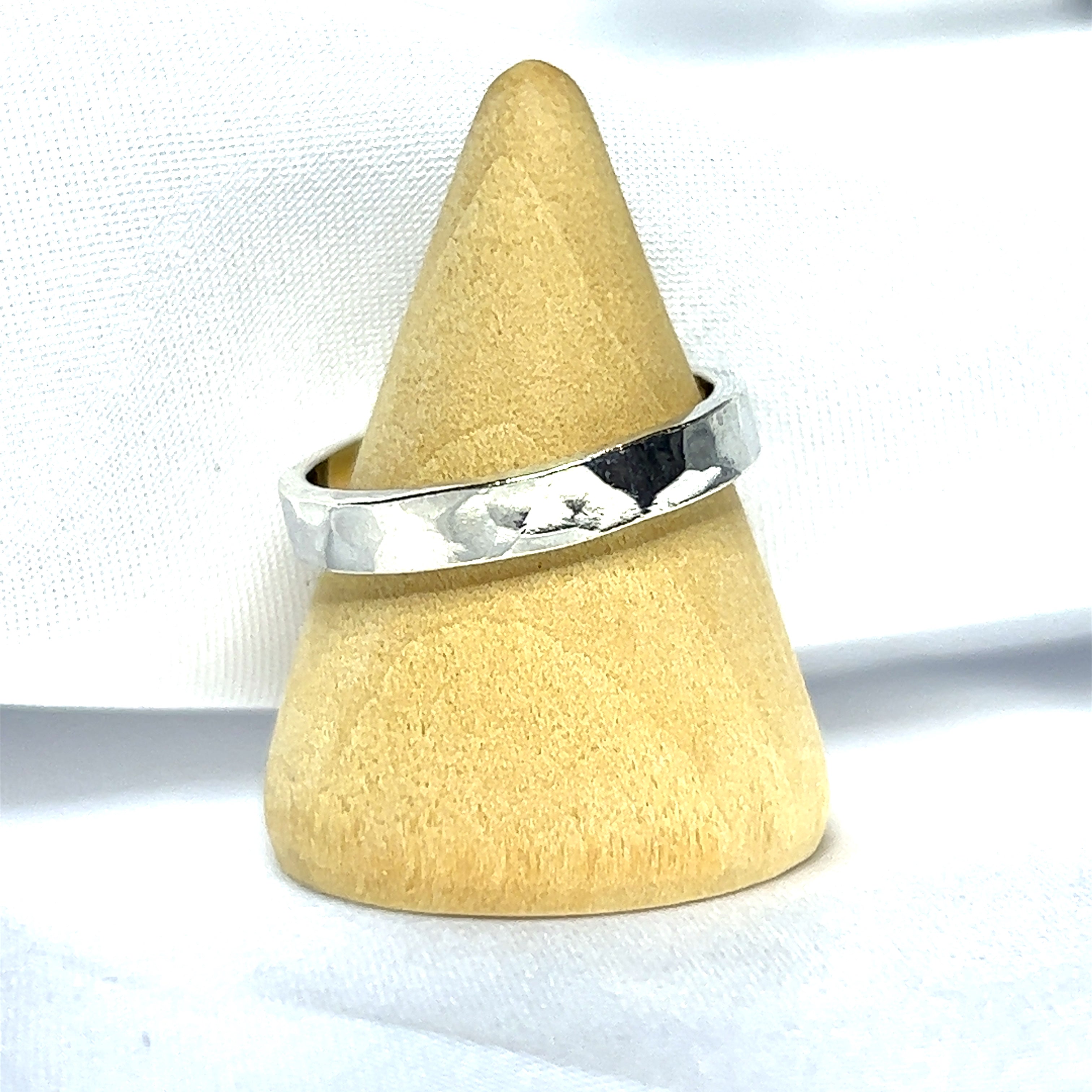 A Super Silver ring with a 3mm Flat Hammered Band sitting on top of a wooden cone, adding a contemporary twist to its rustic allure.