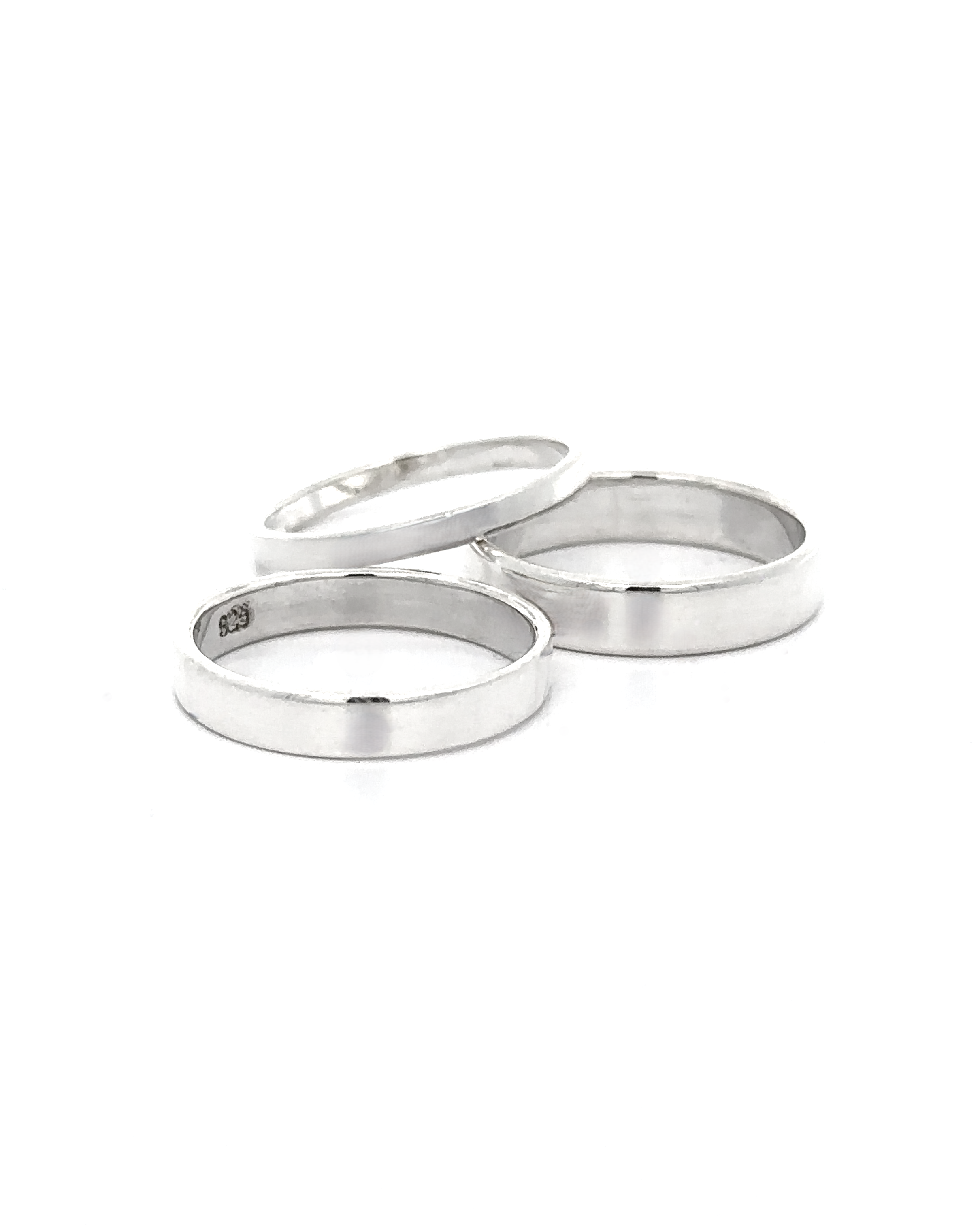 Three Minimalist Flat Band Rings in sterling silver are displayed on a white background, two lying flat and one at an angle—a perfect accessory for any minimalist style.