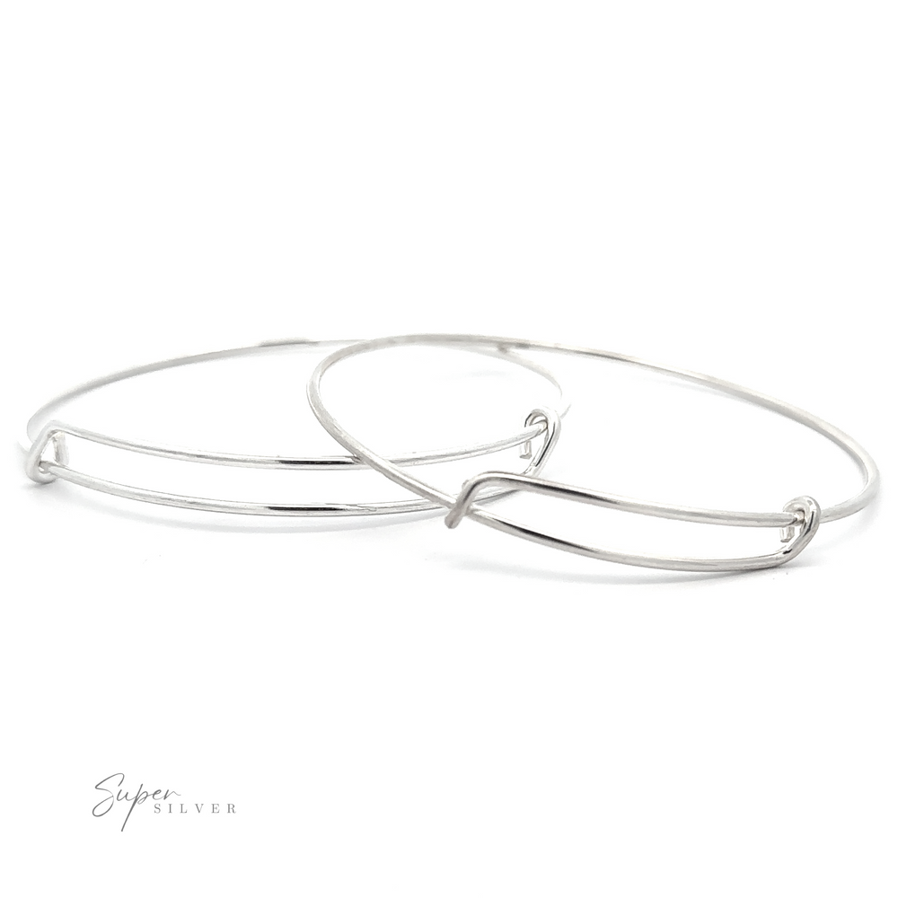 Two thin, sterling silver bangles are slightly overlapping on a white background. One bangle has a minimalist design with a subtle twist detail. The 