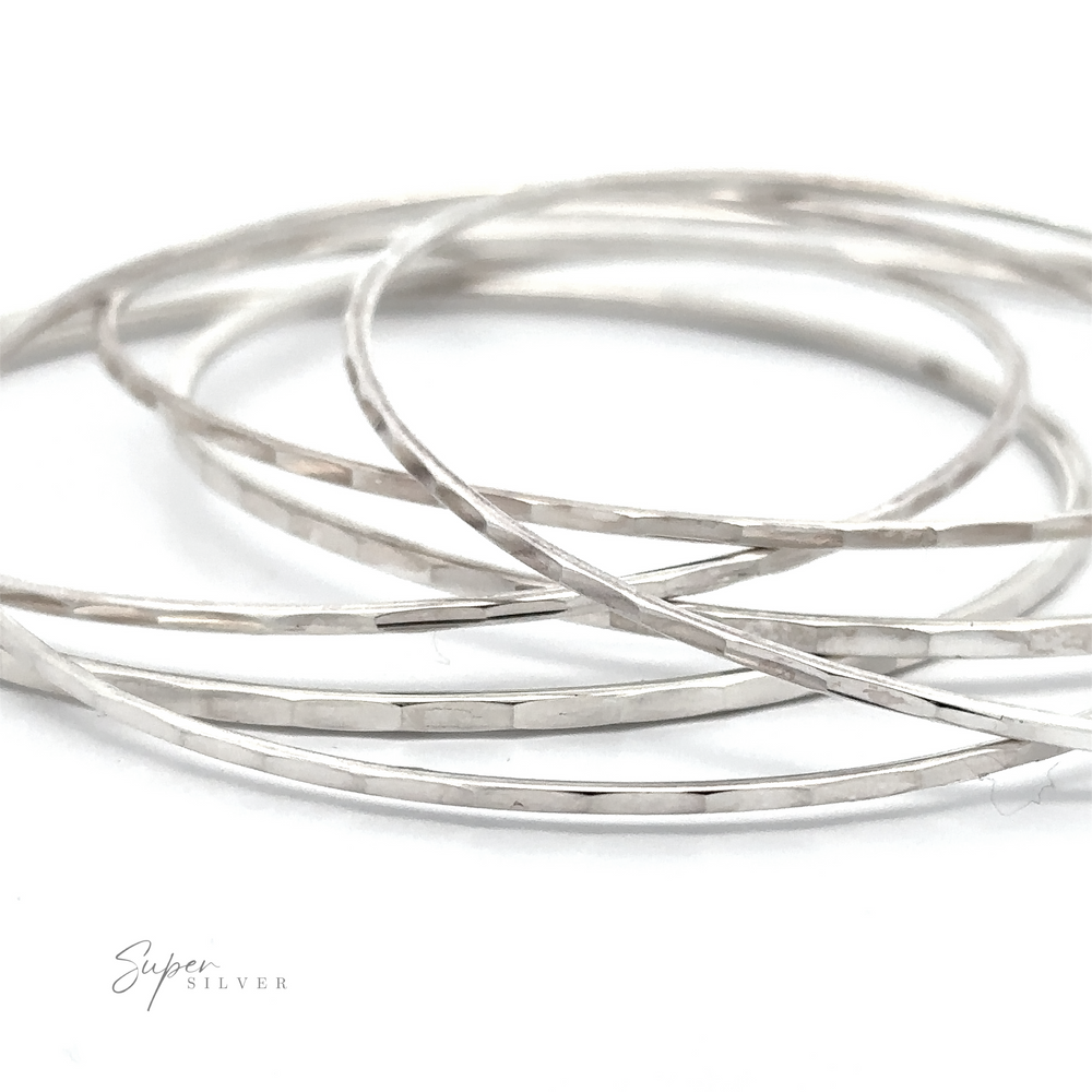 Multiple thin Faceted Silver Bangle Bracelets are intertwined and laid out against a white background, with the words 