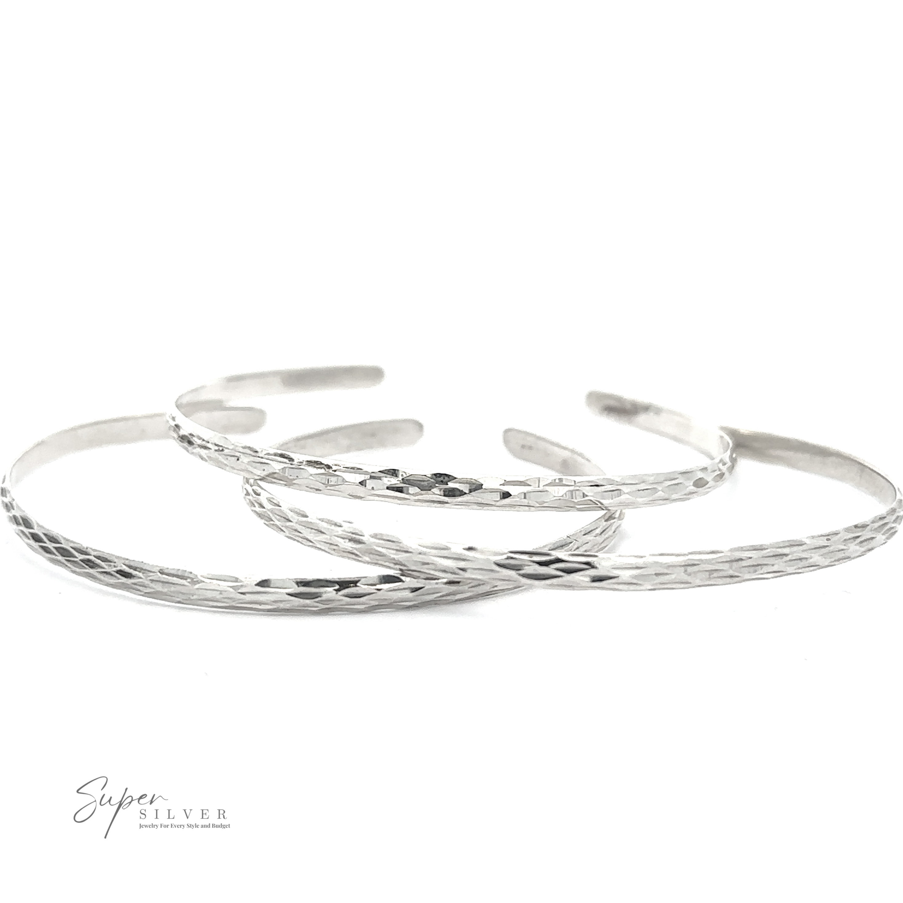 Three overlapping, thin, sterling silver bracelets with a textured pattern. The logo “Glittering Diamond Cut Cuff Bracelet” is displayed in the bottom left corner. These minimalist bracelets offer a subtle elegance perfect for any occasion.