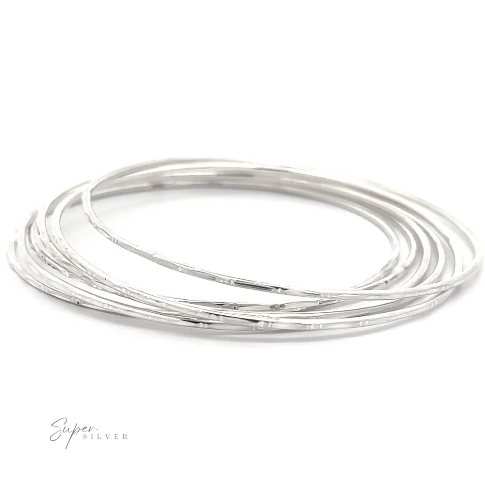 Thin silver bangles stacked together with the "Delicate Faceted Cut Bangle Bracelet" logo in the bottom left corner, featuring a delicate faceted bamboo cut for a touch of elegance.
