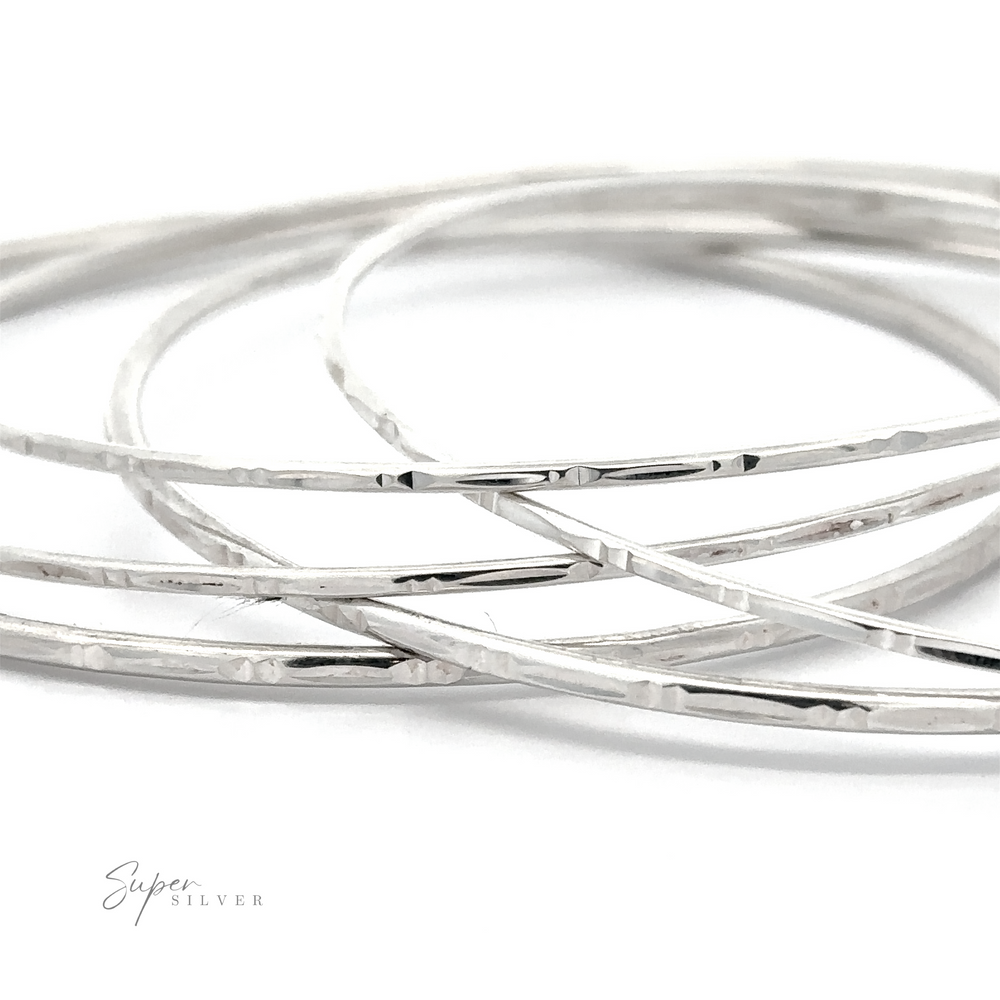Close-up of several thin, textured, sterling silver bangles overlapping each other. 