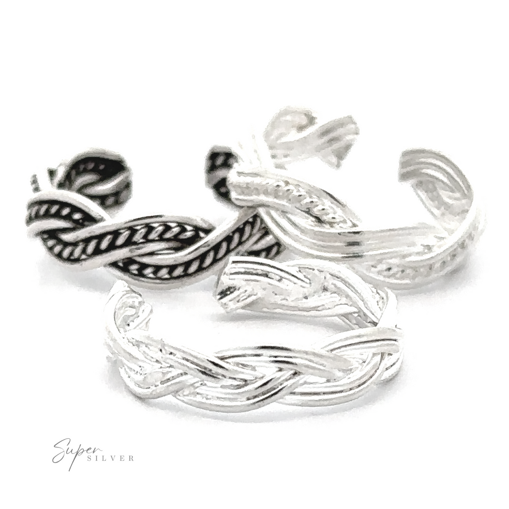 Close-up of three intertwined Various Braided Adjustable Toe Rings with intricate patterns, displayed on a white background with a subtle signature at the bottom right.