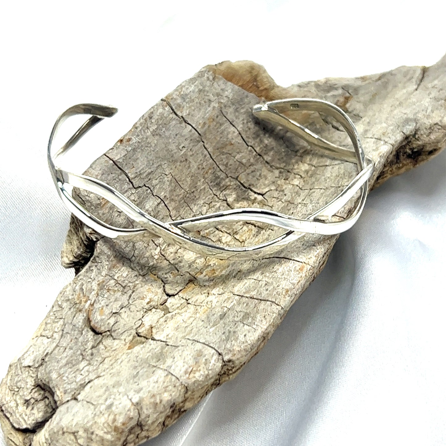 
                  
                    A Super Silver Stylish Twisted Silver Cuff bracelet with a twisting pattern, resting on a piece of wood.
                  
                