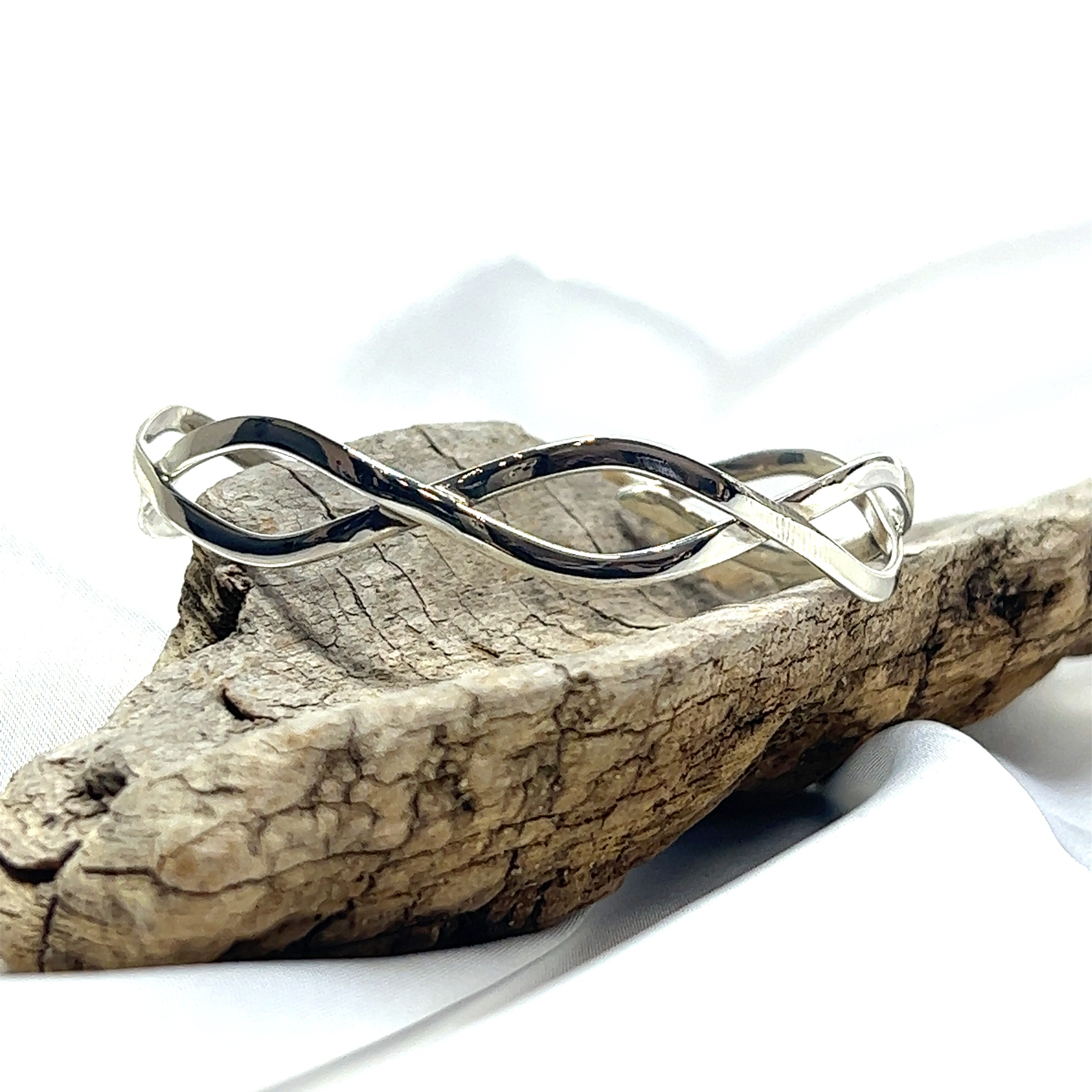 A Super Silver Stylish Twisted Silver Cuff with a twisting pattern sitting on top of a piece of wood.