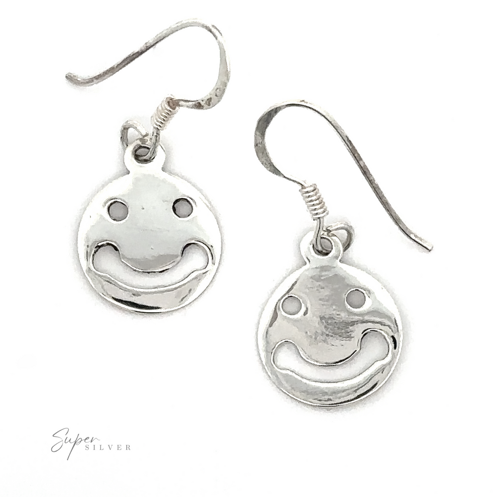 A pair of Smiley Face Earrings with hook fastenings, isolated on a white background, with a signature at the bottom right.