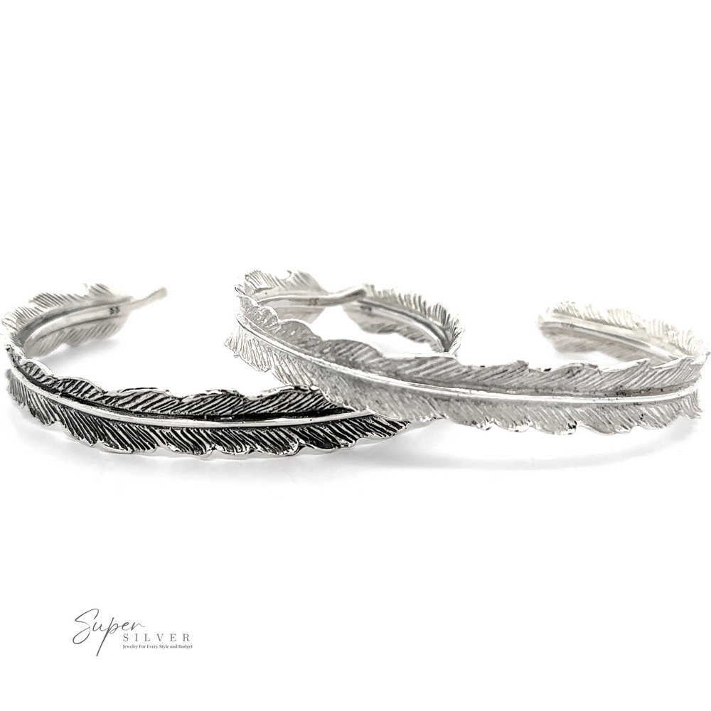 
                  
                    Two .925 sterling silver Detailed Feather Cuff bracelets with intricate detailing, one darker and other lighter in color, positioned side by side on a white background. The oxidized feather cuff design adds a vintage feel. The logo "Super Silver" is visible in the bottom left corner.
                  
                