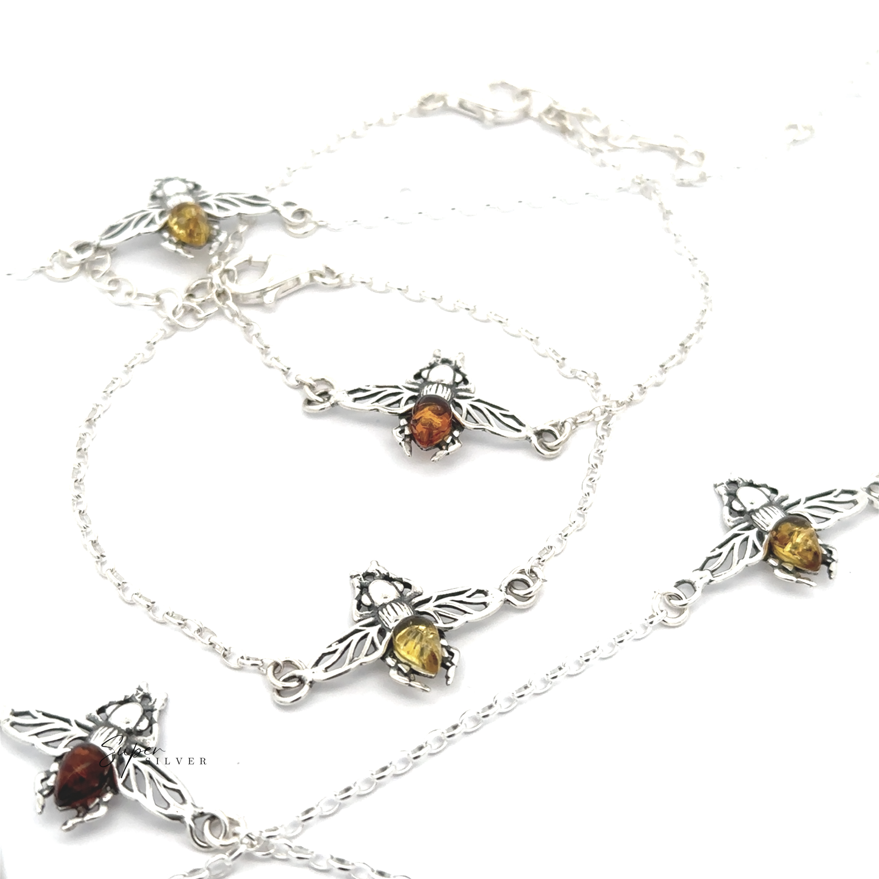 The Baltic Amber Bee Bracelet, a sterling silver chain adorned with bee-shaped charms featuring Baltic amber and yellow gemstone bodies, is elegantly displayed on a white background.