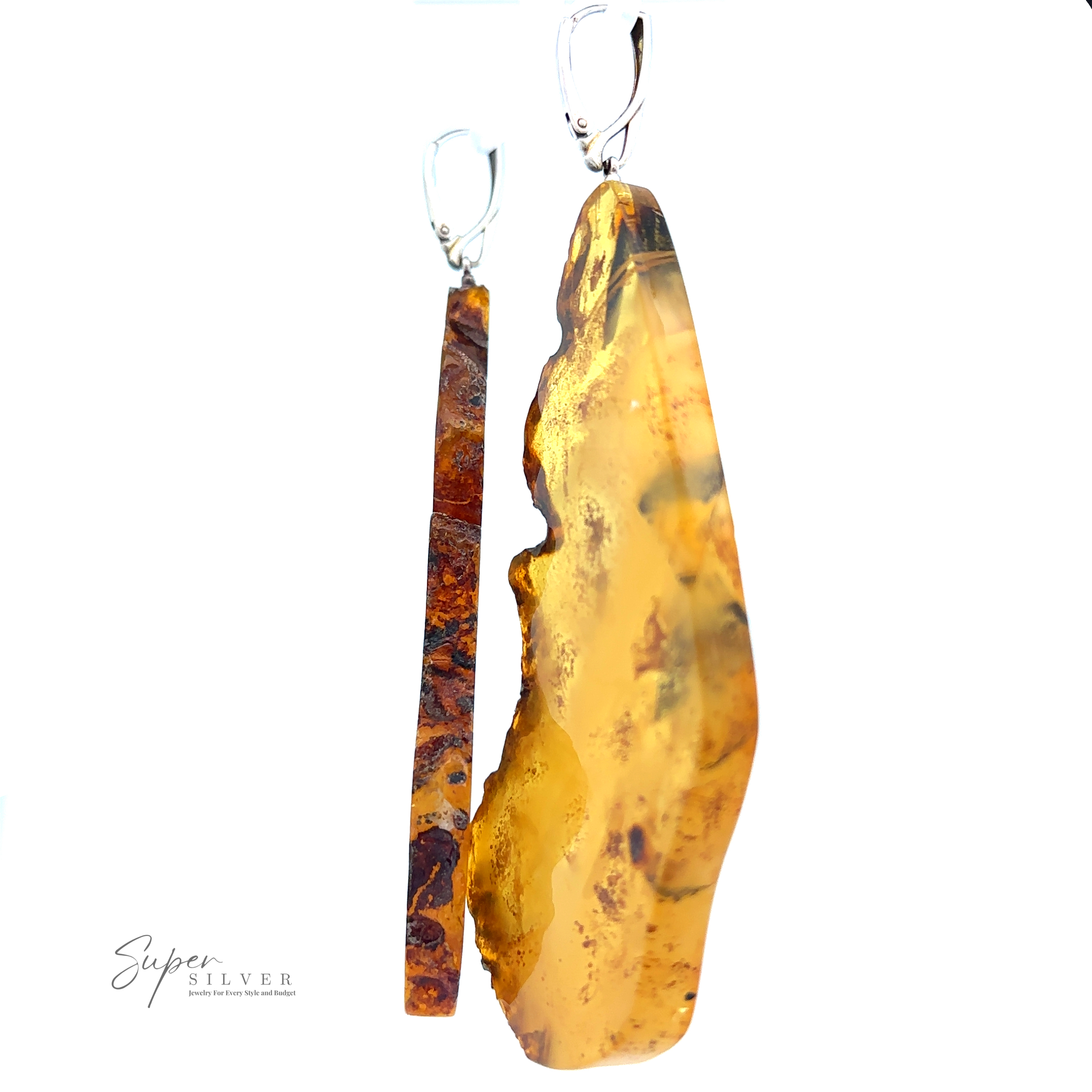 Two handcrafted pendants displayed against a white background. The left pendant is thin and brown with a rugged texture, while the right pendant features Designer Raw Cognac Amber Slab Earrings, larger, translucent yellow, and smoothly polished.