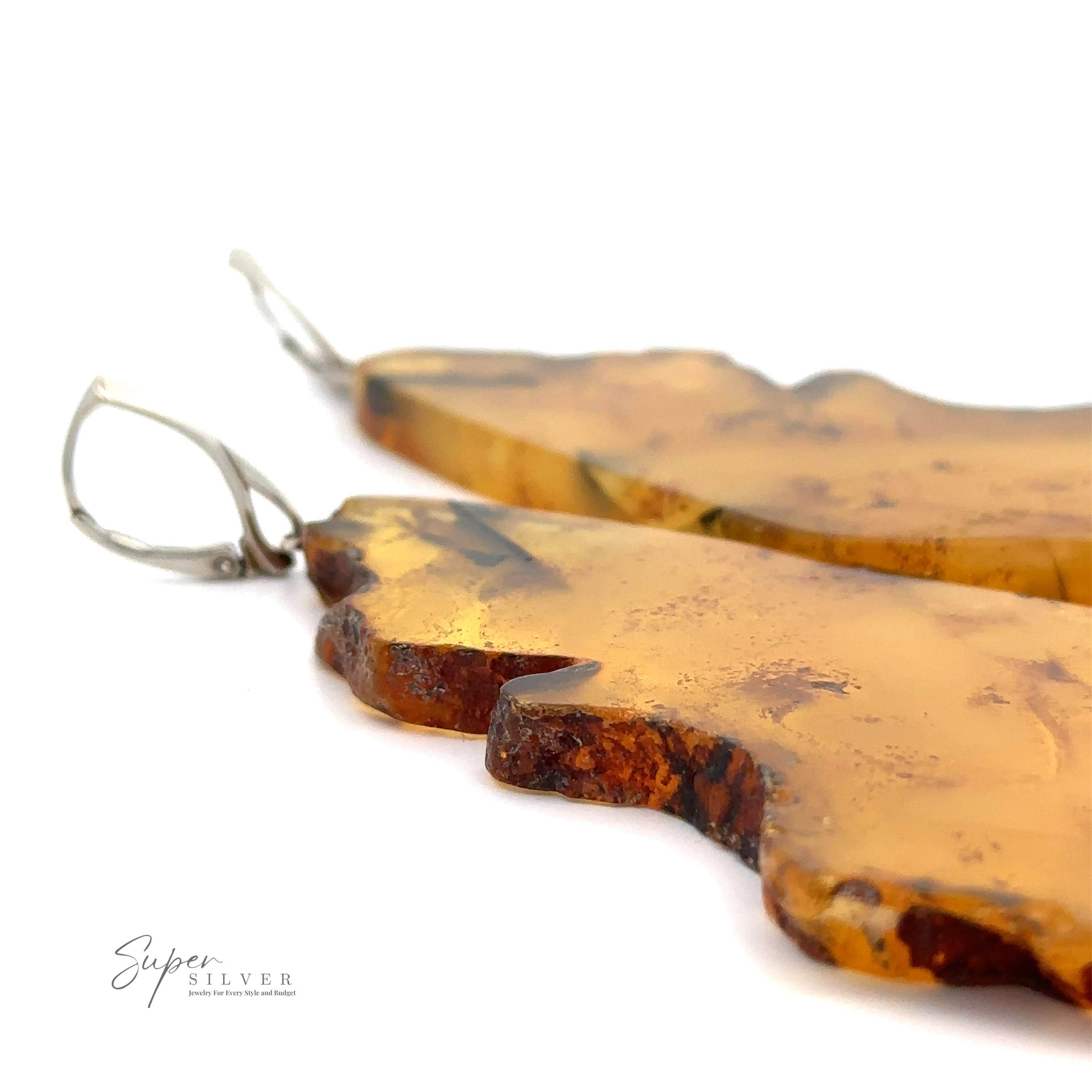 Close-up image of two irregularly shaped Designer Raw Cognac Amber Slab Earrings with Sterling Silver hooks on a white background.