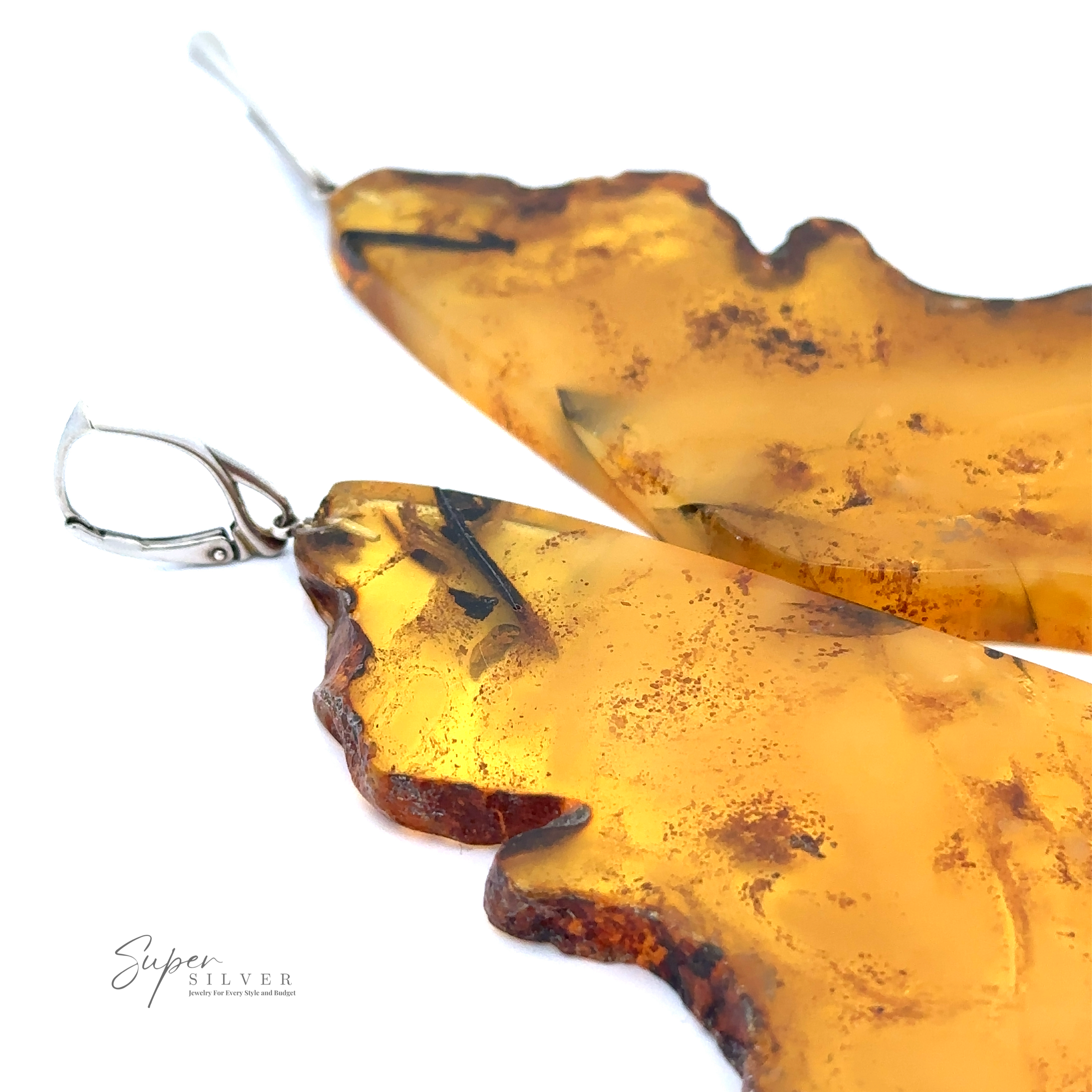 Close-up of a pair of uniquely-shaped Designer Raw Cognac Amber Slab Earrings with sterling silver clasps. A small logo in the corner reads "Super Silver.