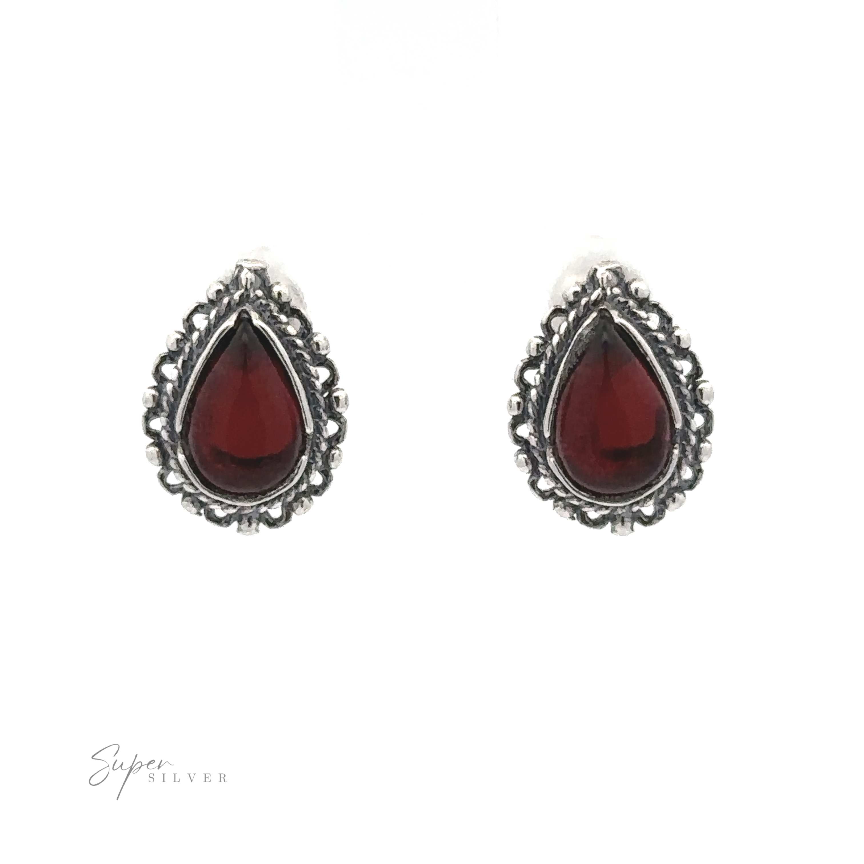 A pair of Framed Teardrop Amber Studs featuring dark red gemstones bordered with intricate silver detailing, displayed on a white background, exuding a sense of vintage romance.