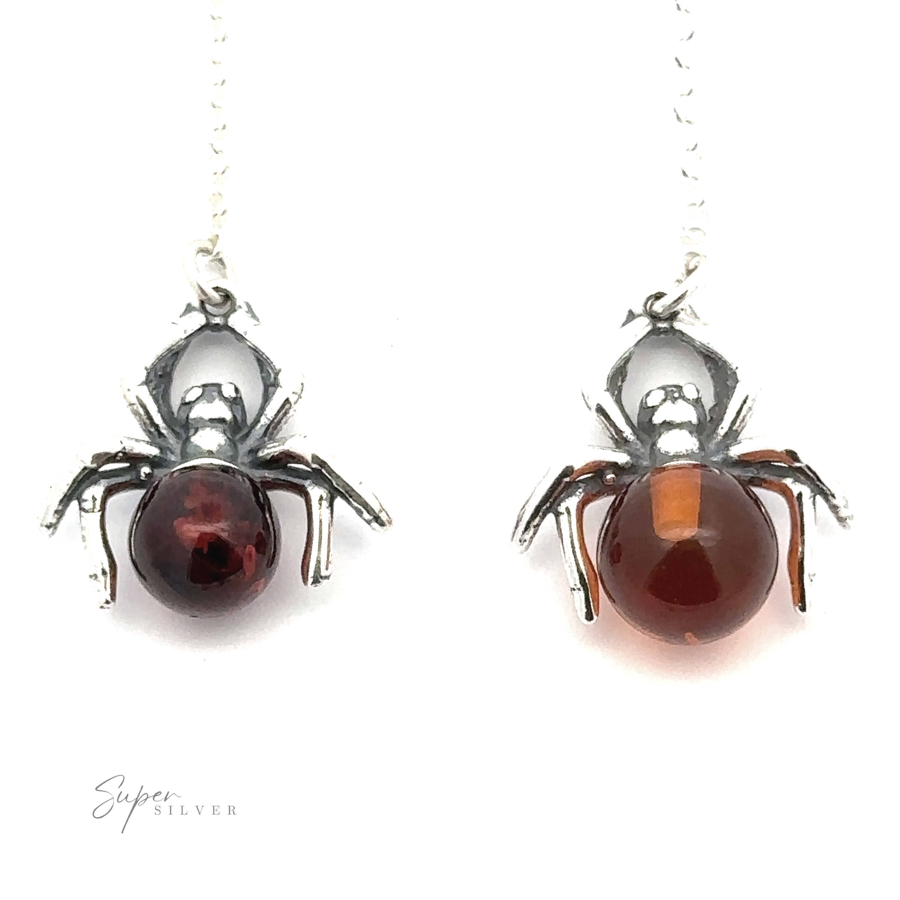 Two silver-colored spider-shaped pendants with gemstone bodies exude a witchy vibe; the one on the left has a dark red stone, while the one on the right features Baltic amber. The chain is partially visible. This product is called the Baltic Amber Spider Necklace.