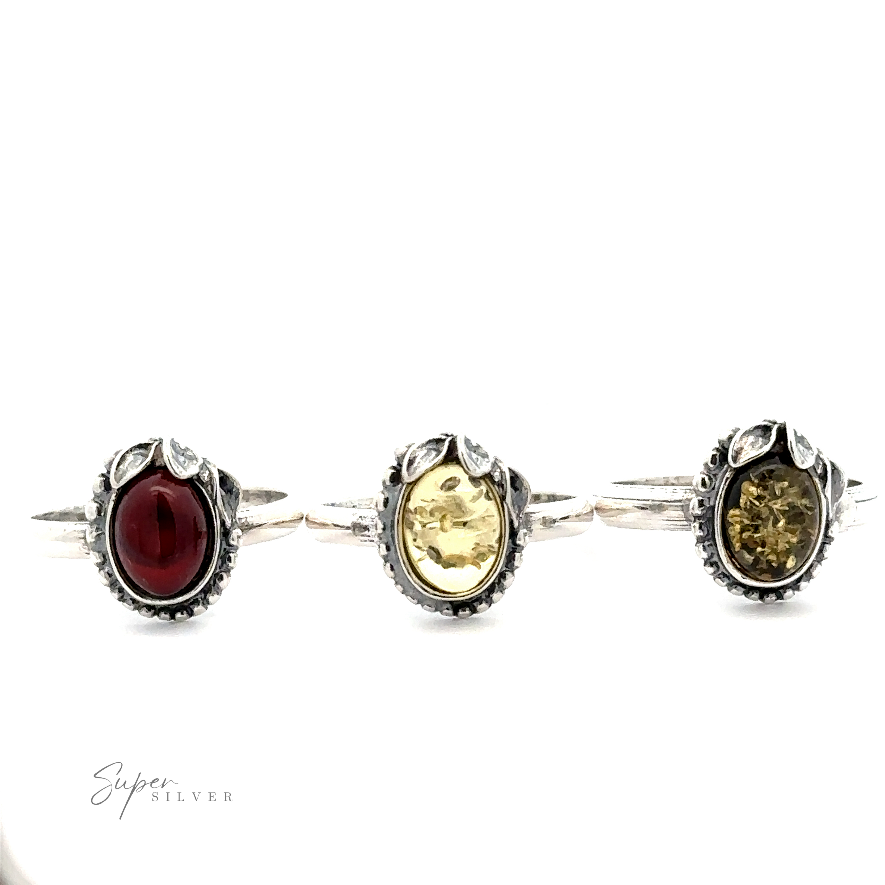 Three silver rings with ornate settings exude vintage elegance; the left ring has a red gemstone, the middle features an Amber Ring with Beaded Border and Peace Lily Details, and the right showcases another yellow gemstone. "Super Silver" text in the bottom left.