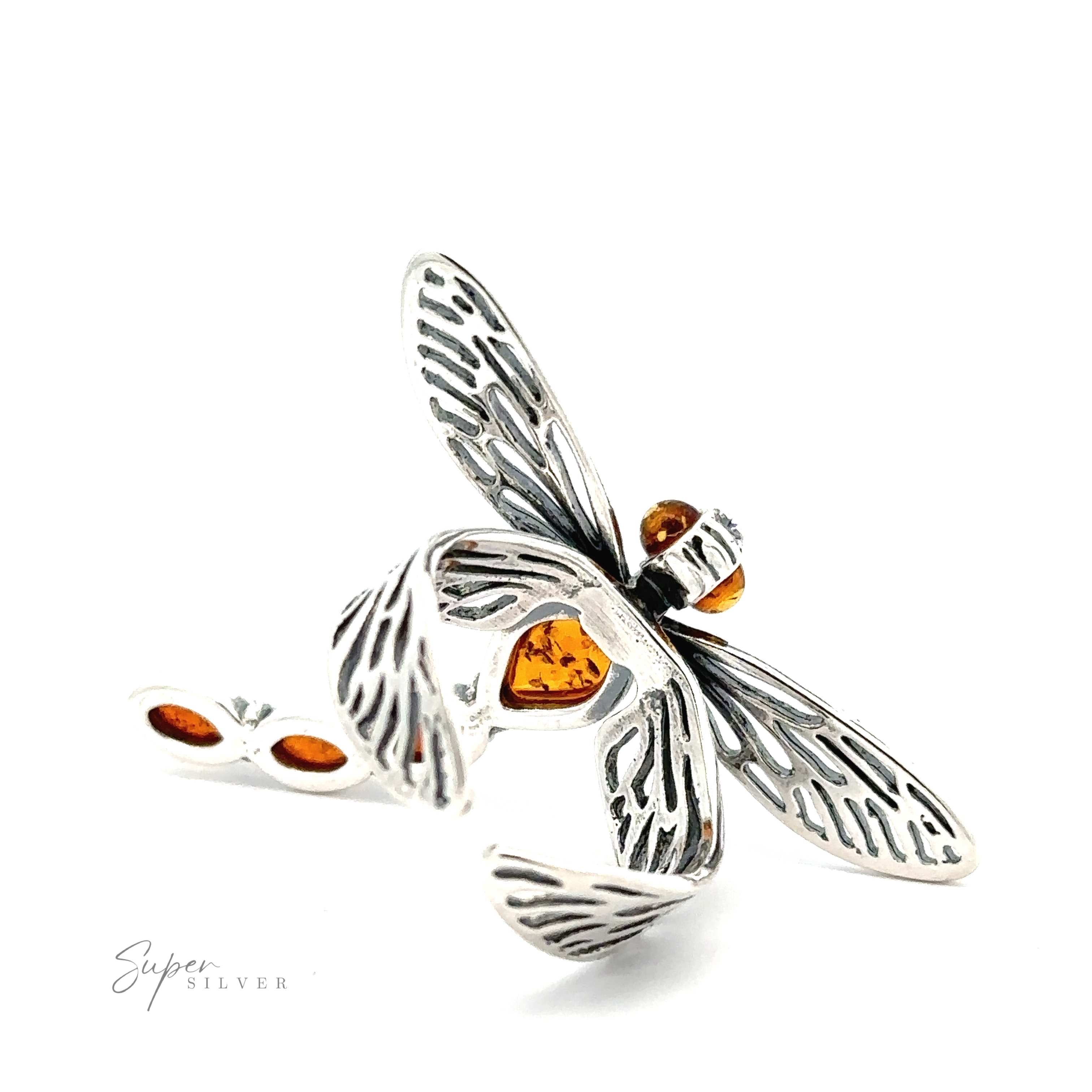 A silver dragonfly-shaped pendant with detailed wings and cognac amber gemstone accents is displayed on a white background. Text reads "Amber Dragonfly Adjustable Ring.