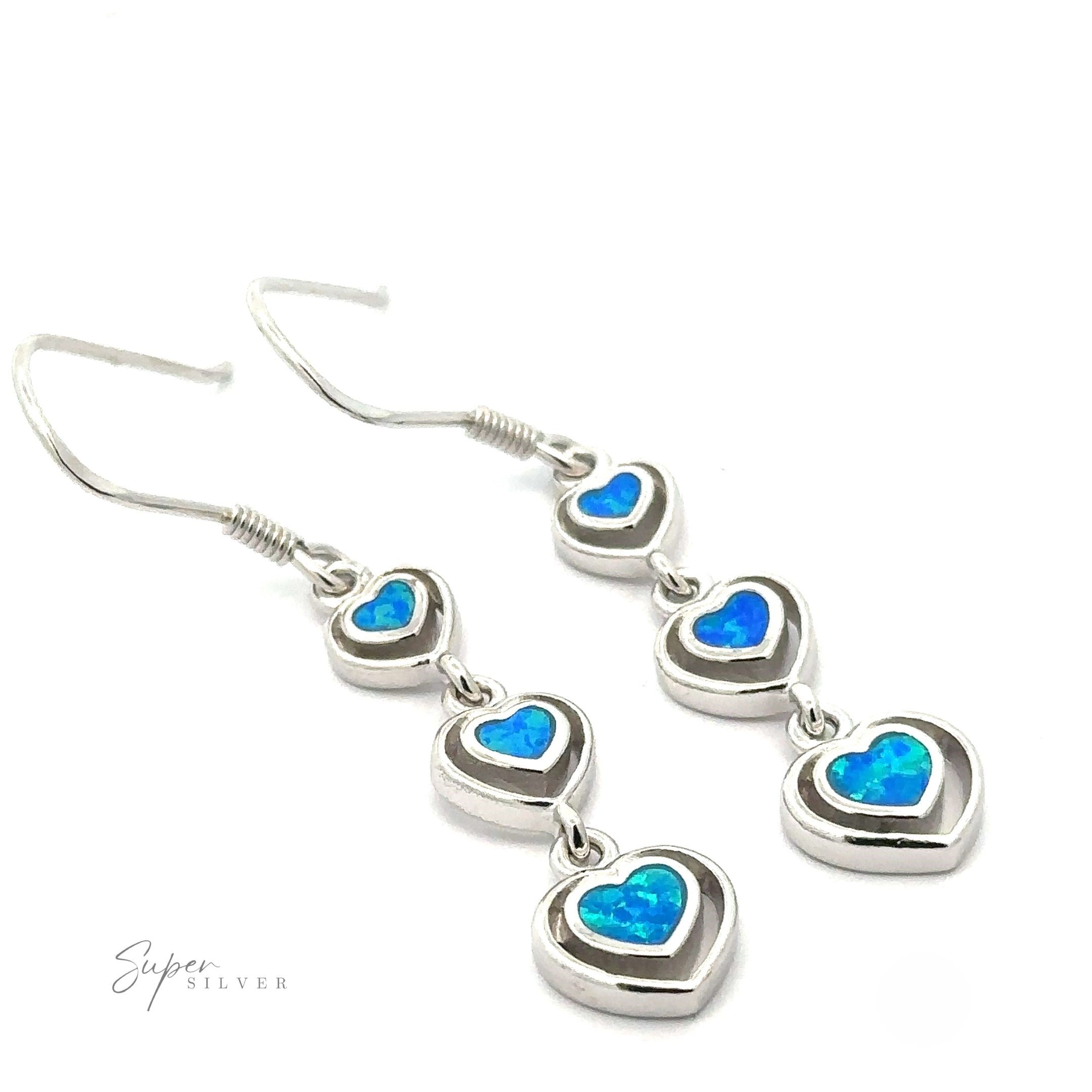 A pair of "Dangling Lab-Created Opal Heart Earrings" features sterling silver, heart-shaped designs with lab-created blue opal inlays, showcasing three hearts on each earring and attached to hooks for wearing.