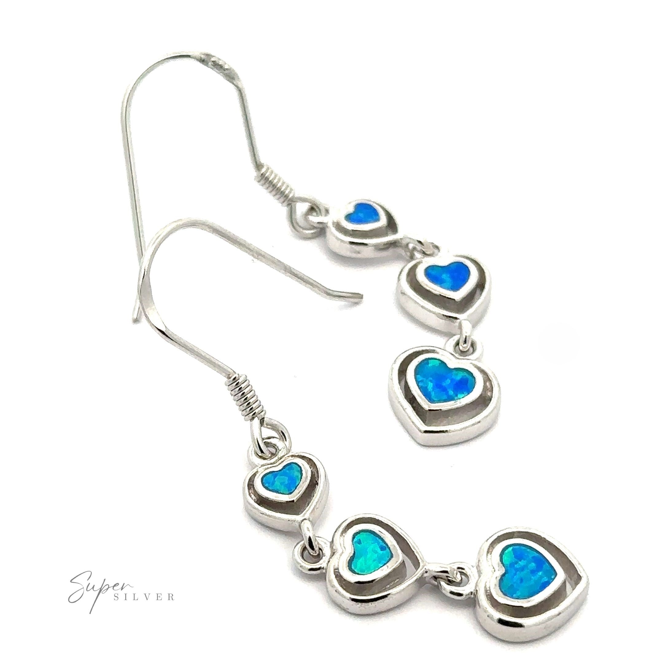 The Dangling Lab-Created Opal Heart Earrings feature three linked, heart-shaped blue stones. These stunning sterling silver drop earrings are gracefully displayed against a white background.