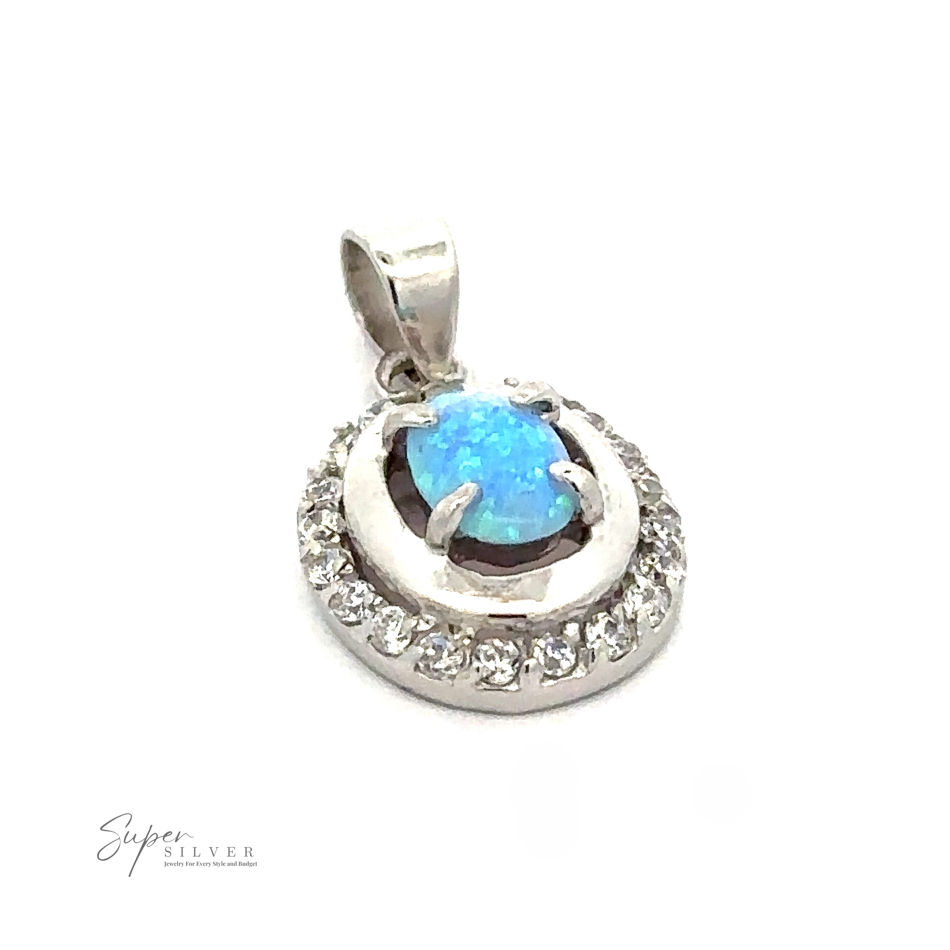 A silver pendant featuring an oval blue lab-created opal gemstone surrounded by a ring of small clear cubic zirconia stones. The pendant has a simple bail for attaching to a necklace, making it a timeless piece of Art Deco jewelry. The "Opal Pendants with Cubic Zirconia" logo is also visible.