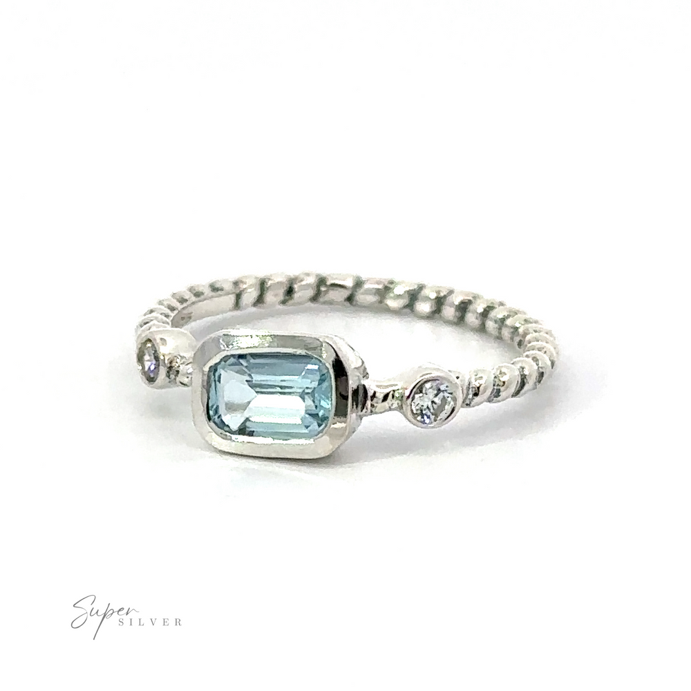 
                  
                    Rectangle Gemstone Ring with Twisted Band with a central aquamarine stone flanked by two smaller diamonds on a white background.
                  
                