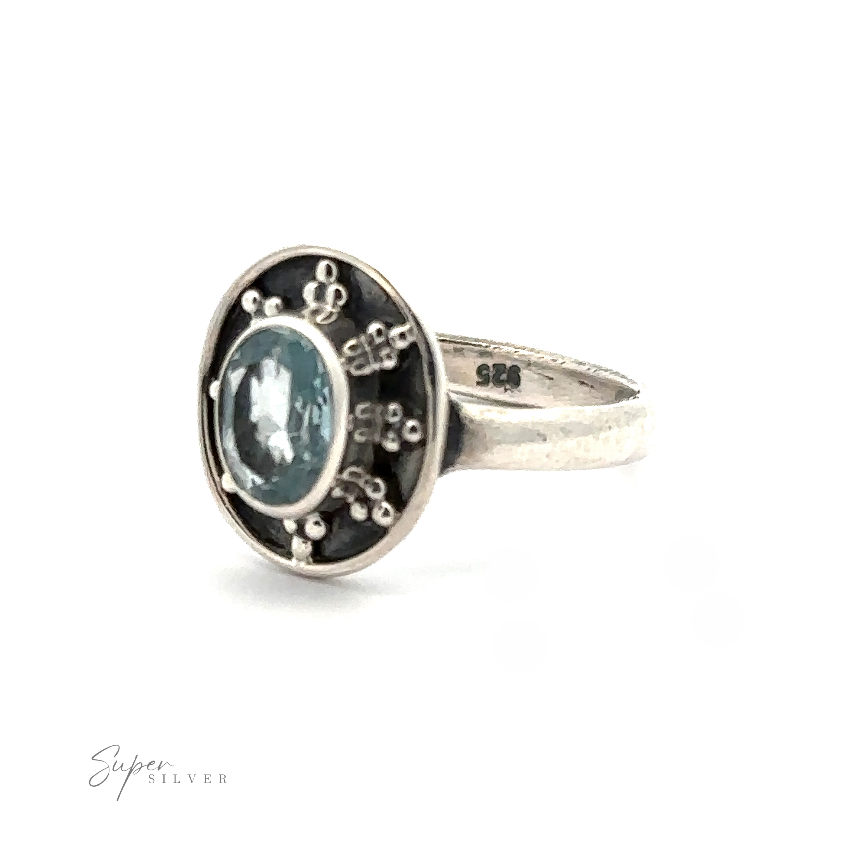 An Oval Gemstone Ring with Ball and Disk Border with a blue gemstone at its center, surrounded by small, intricate designs on a dark background. This vintage-inspired jewelry piece features an inside band inscribed with "925.