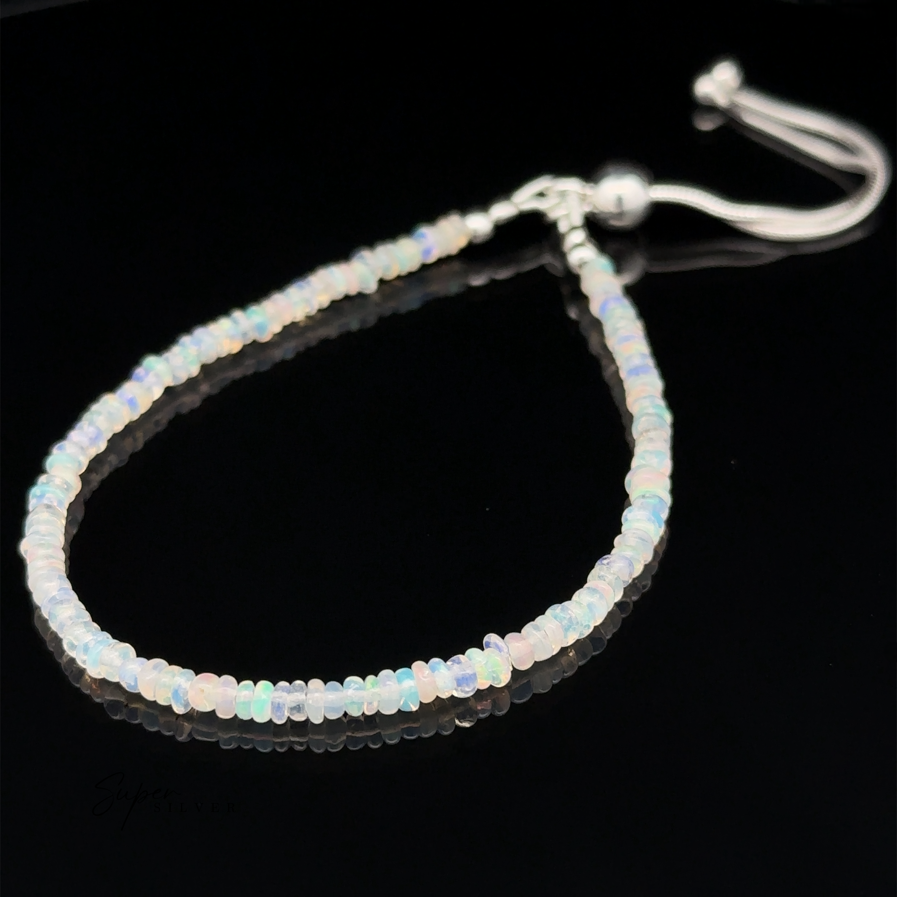 A delicate Ethiopian Opal Beaded Bracelet with an adjustable length closure is displayed on a black surface. The beaded bracelet features small, translucent beads in a variety of soft, iridescent colors.