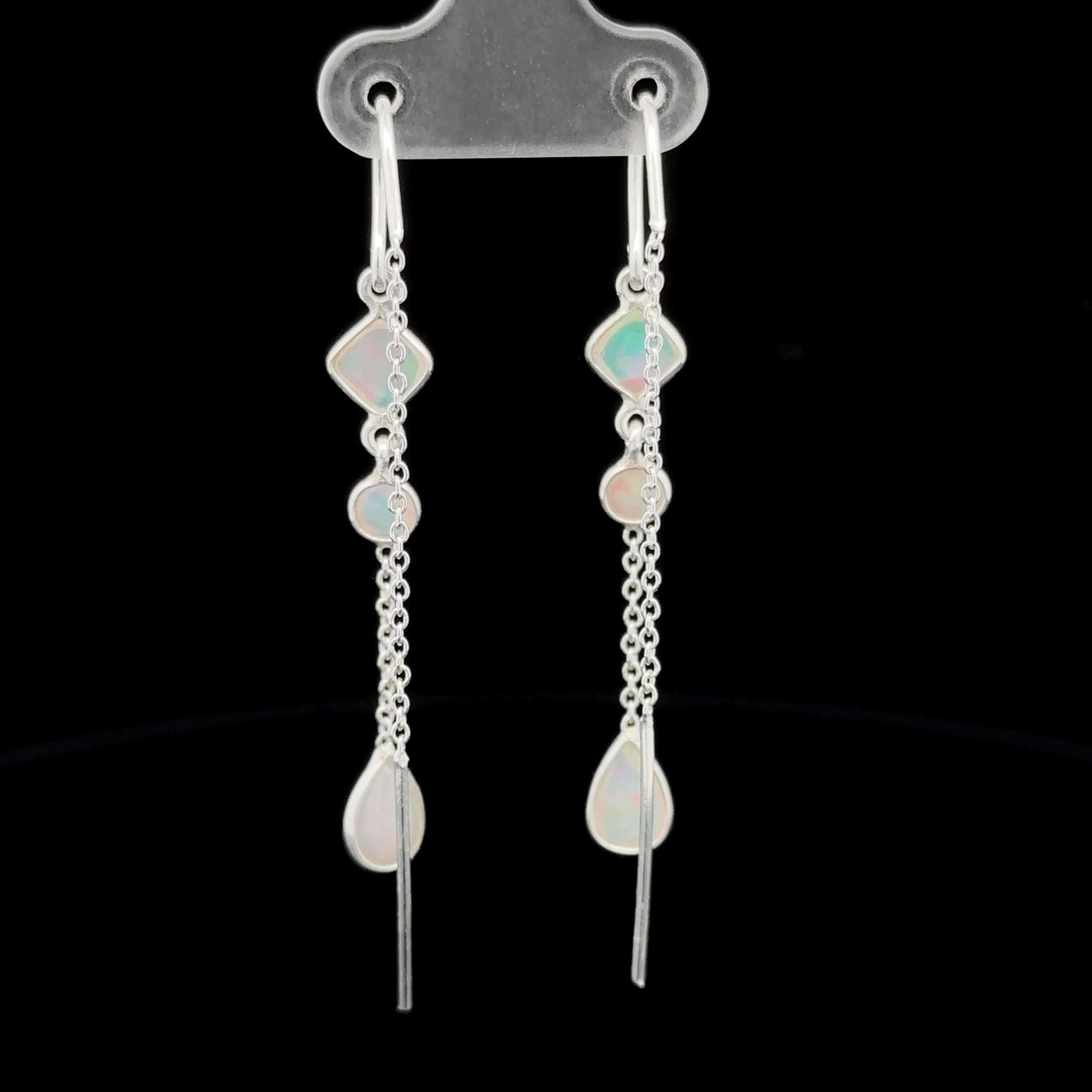 A pair of elegant, long Ethiopian Opal Threader Earrings with multiple geometric stones and chain links, displayed on a clear holder against a black background.