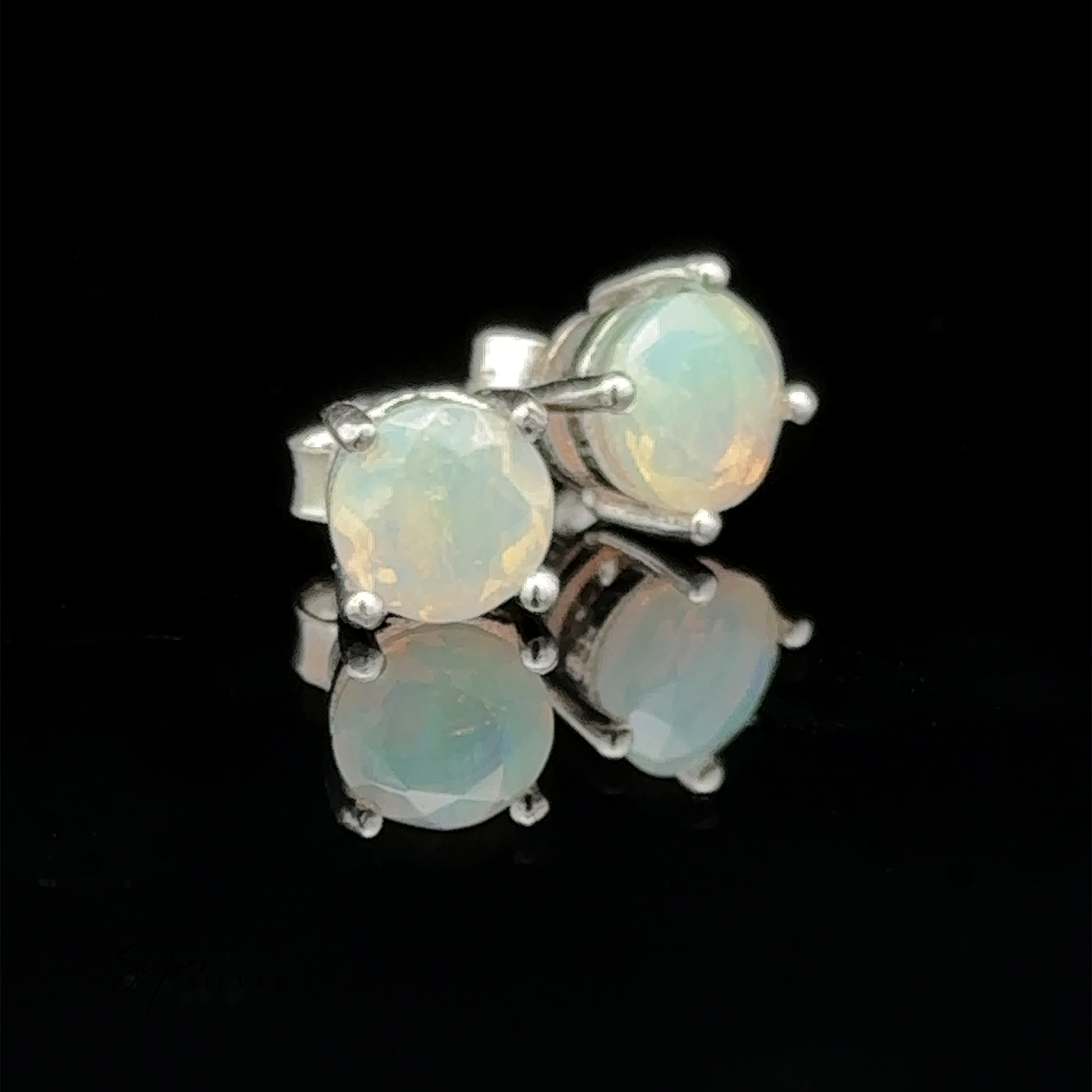 Round Ethiopian Opal Studs, featuring 6mm gems set in sterling silver, are elegantly showcased on a reflective black surface.