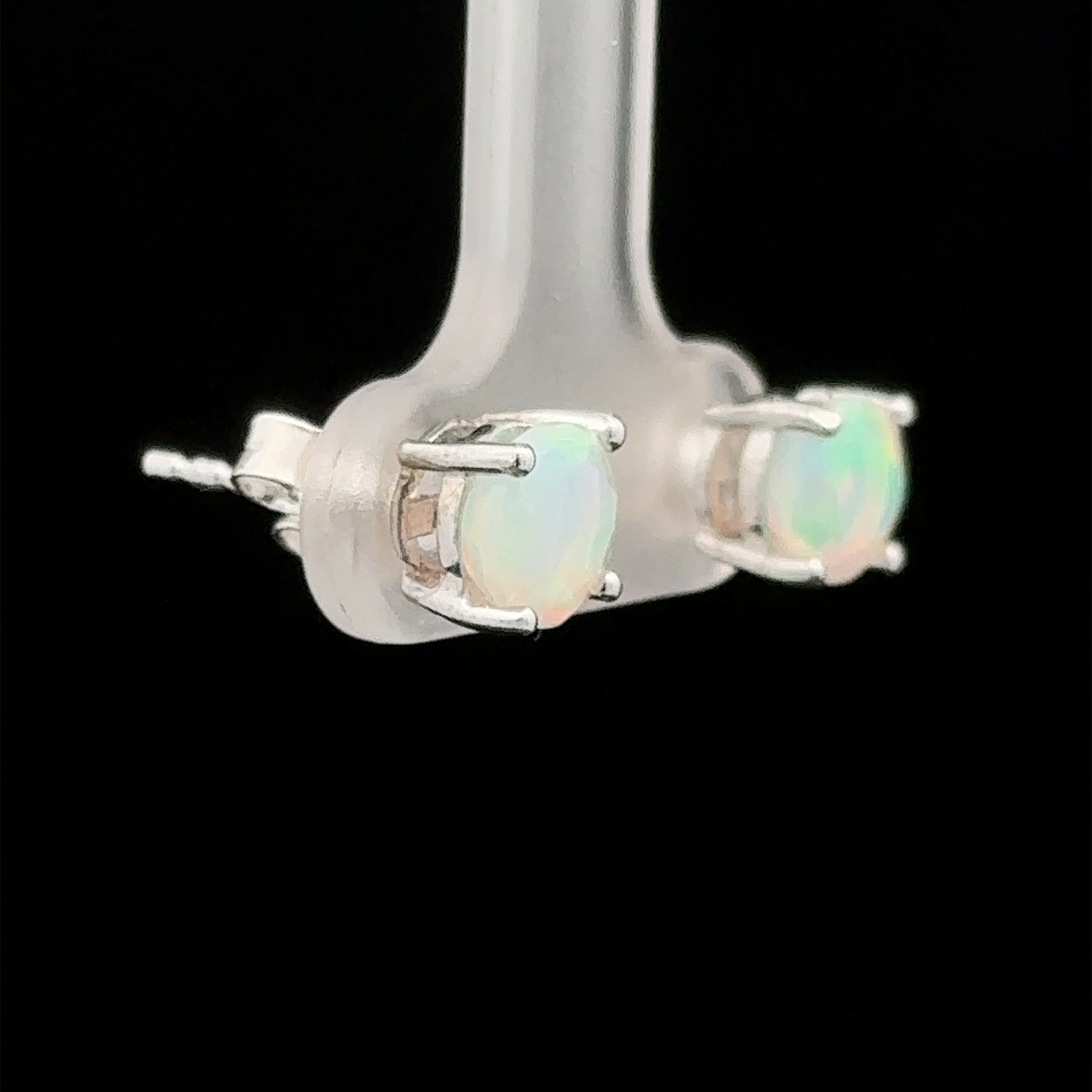 Round Ethiopian Opal Studs with 6mm opals set in sterling silver prongs, displayed on a clear stand against a black background.
