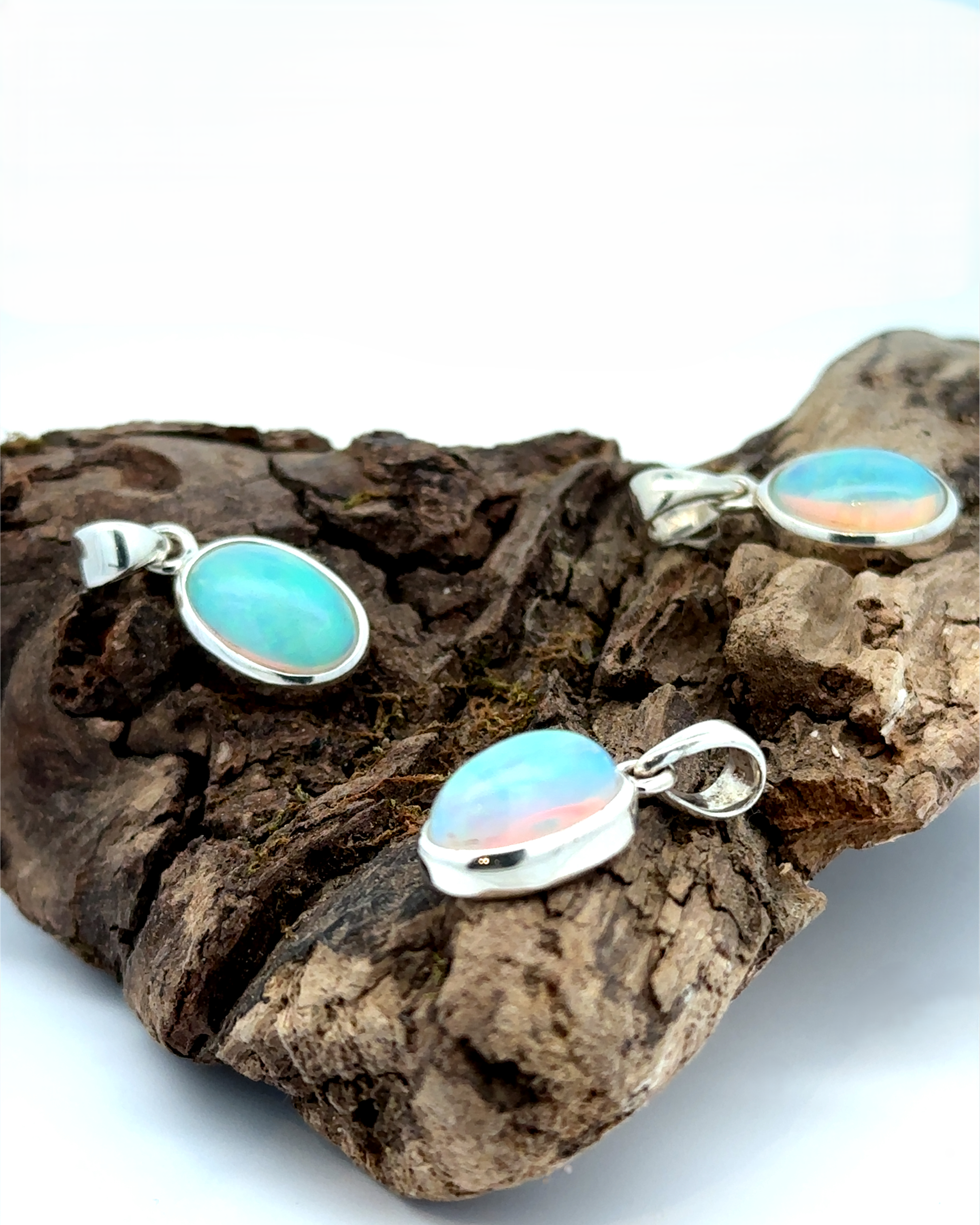 Three Oval Ethiopian Opal Pendants with sterling silver settings are elegantly displayed on a piece of driftwood, embodying a minimalist style.