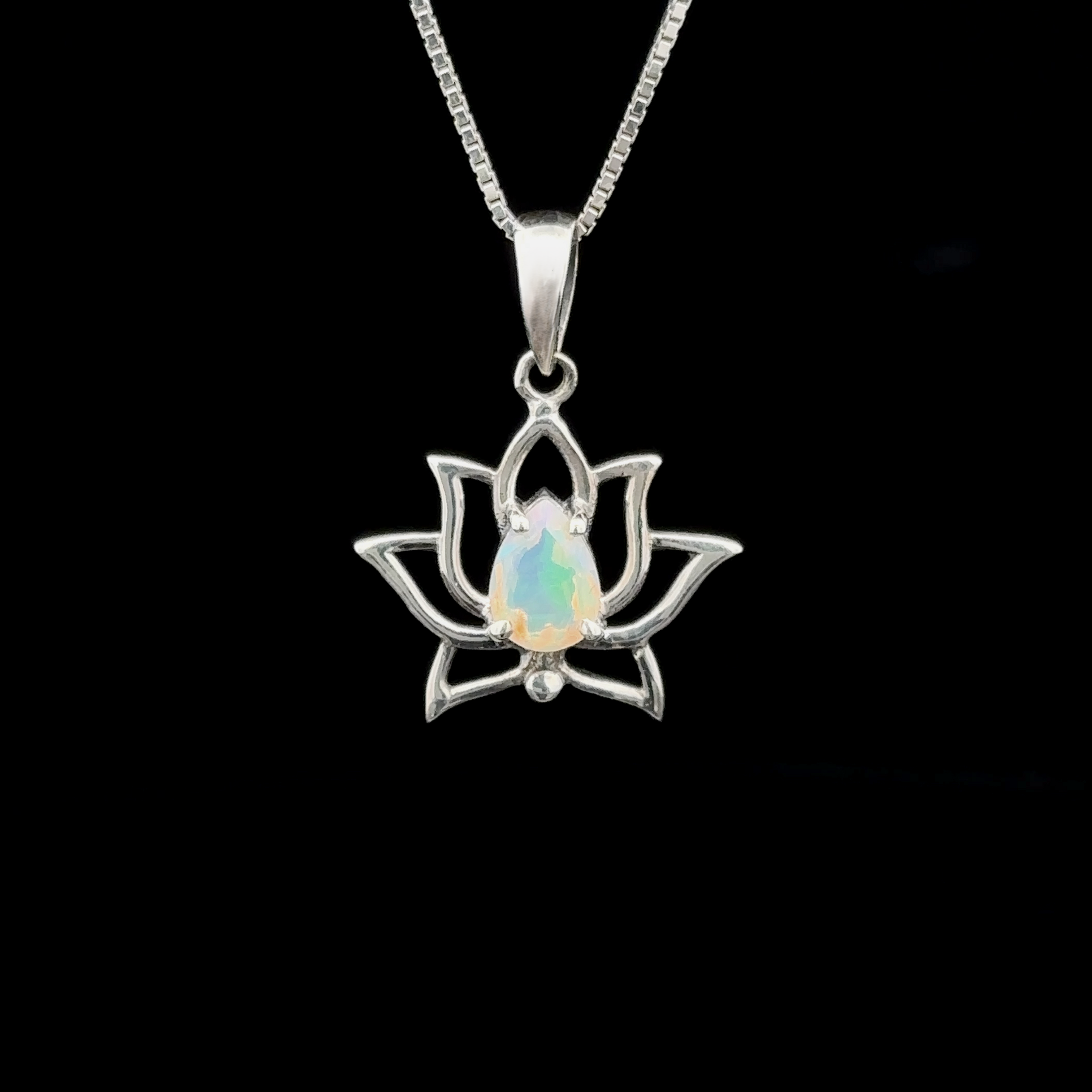 The Ethiopian Opal Lotus Pendant, featuring a sterling silver lotus flower and a central opal gemstone, hangs elegantly from a chain against a black background.