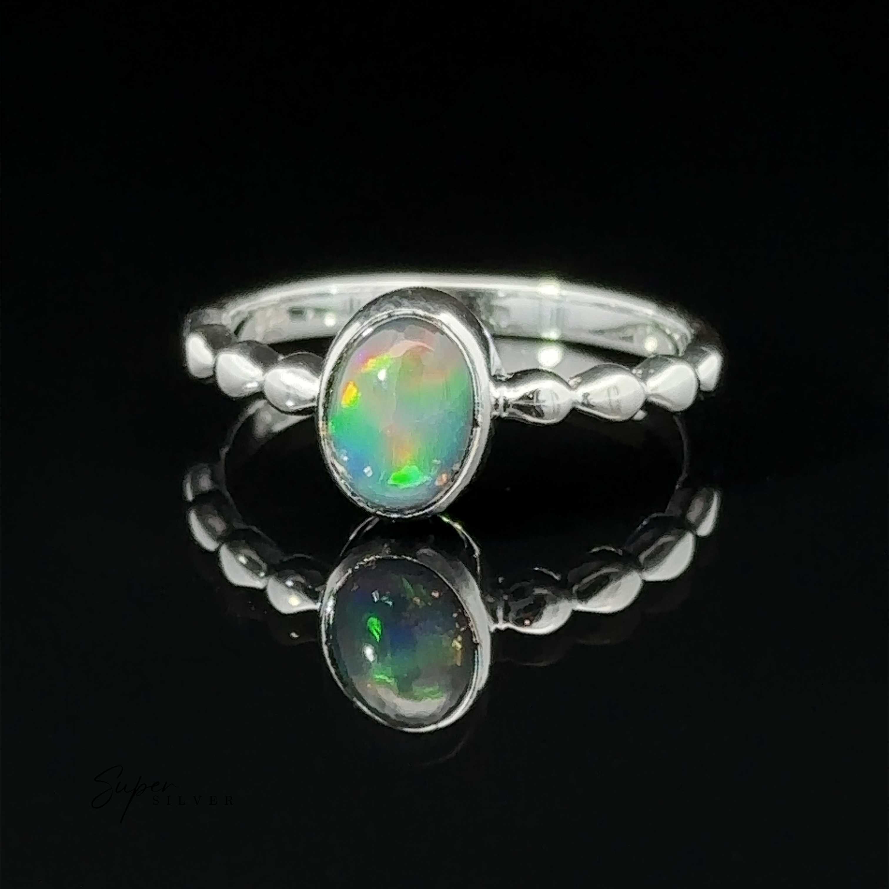 A Oval Gemstone Ring with Beaded Band with an oval opal set in the center, displayed on a reflective black surface showing its reflection.