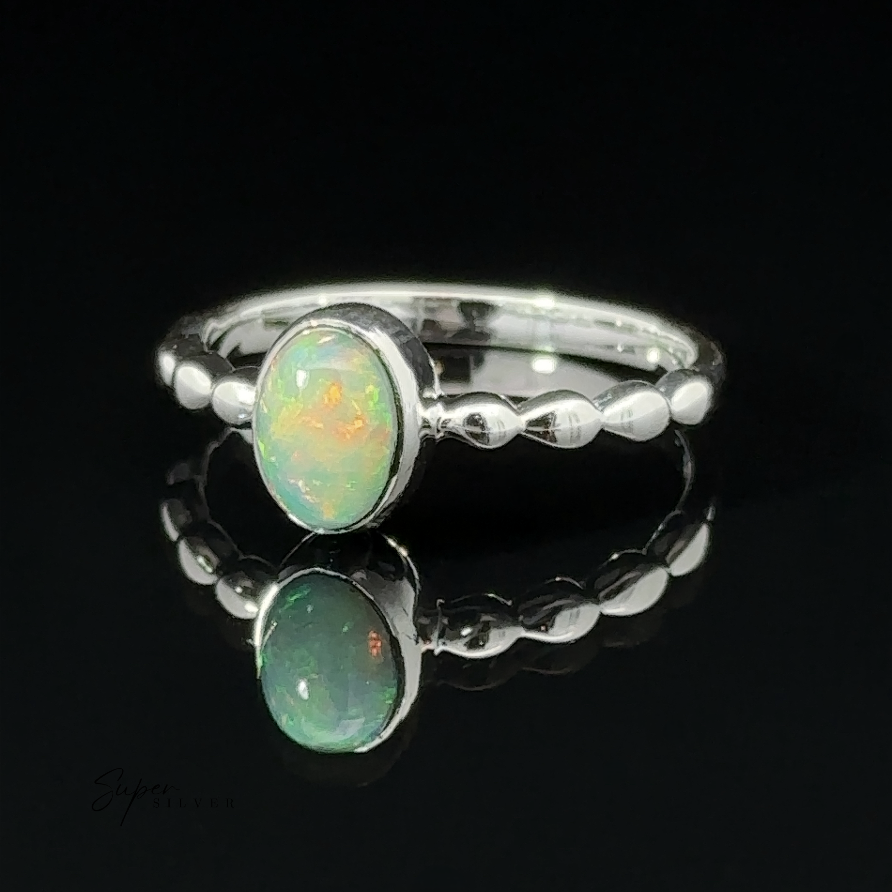Oval Gemstone Ring with Beaded Band with an oval opal stone, displayed on a reflective surface against a dark background.