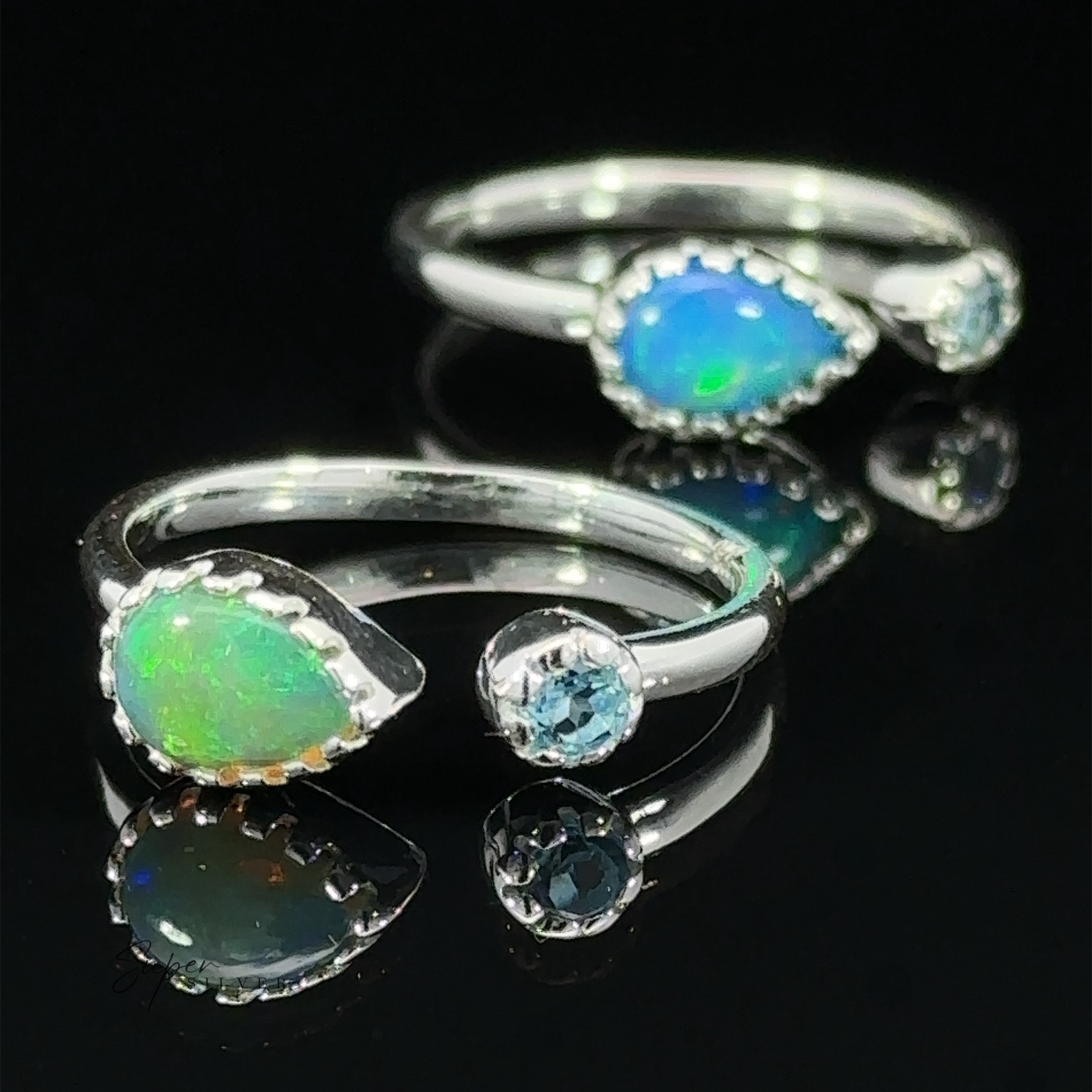 Two dainty adjustable gemstone rings with opal stones and tiny crystals, displayed on a reflective black surface.