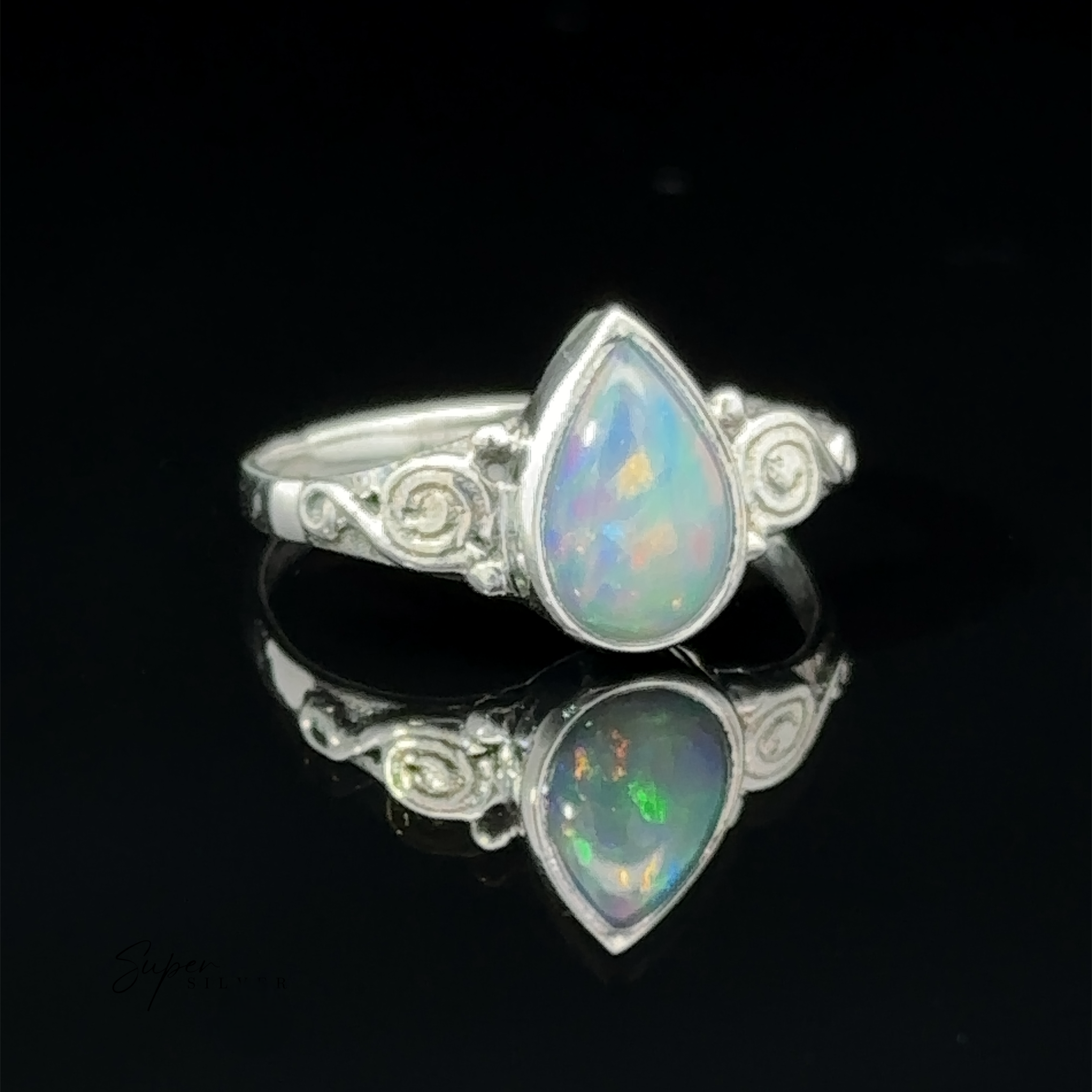 Silver teardrop gemstone ring with colorful speckles, displayed on a reflective black surface.
