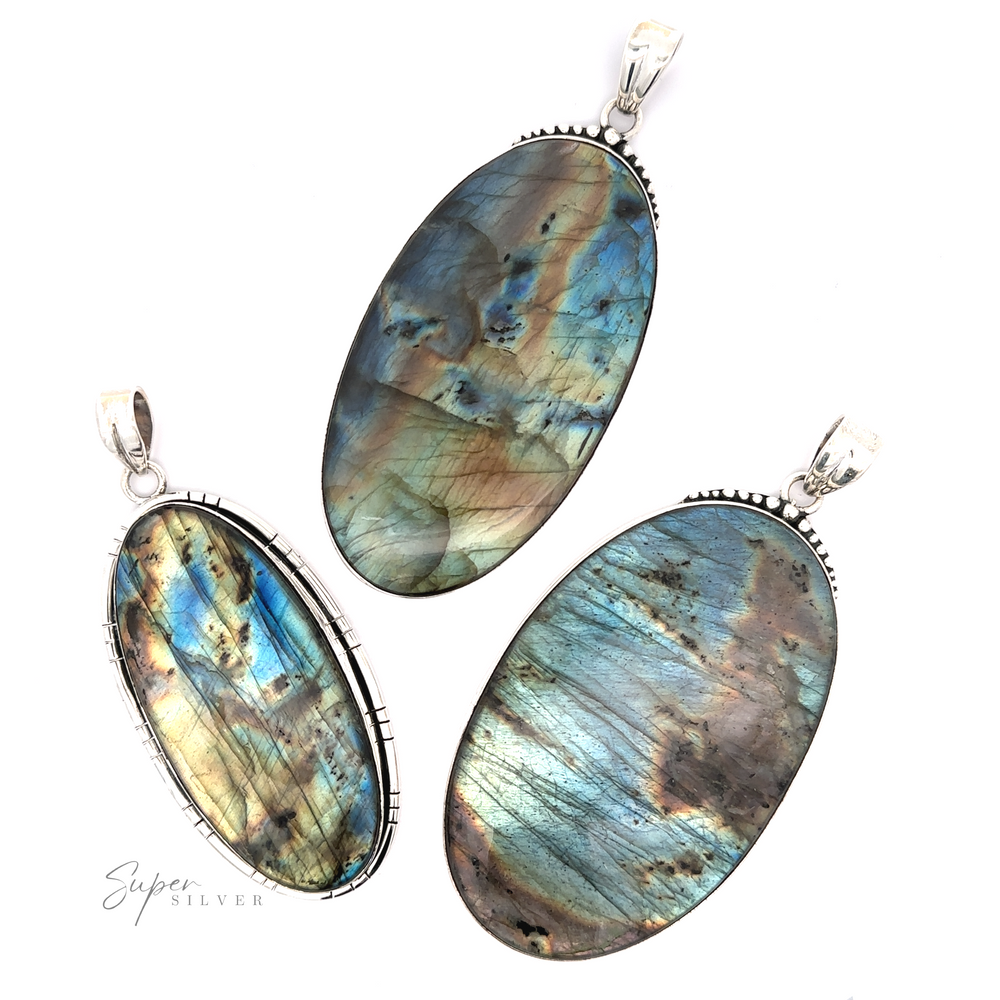 Three XL Statement Oval Labradorite Pendants with silver settings are displayed on a white background. The stones exhibit iridescent blue, green, and brown hues. One pendant features the text "Super Silver," showcasing the beauty of Sterling Silver jewelry.
