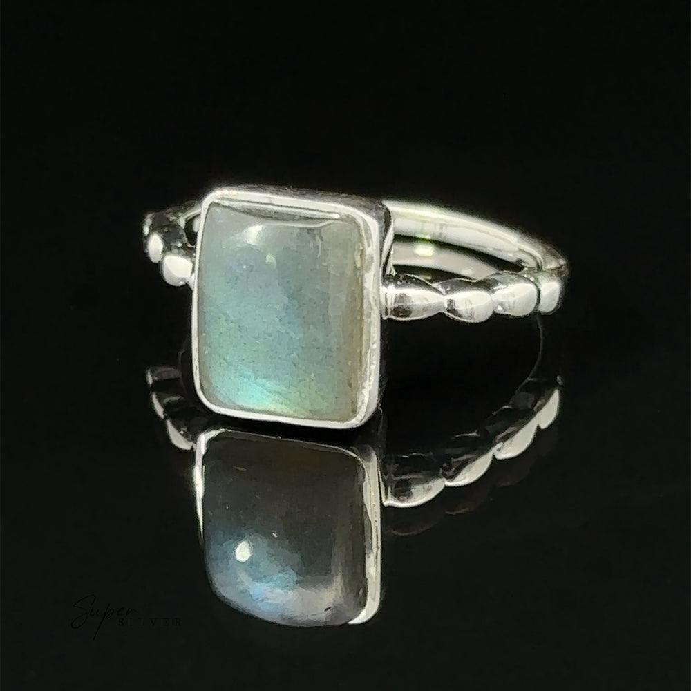 
                  
                    A Rectangle Gemstone Ring with Beaded Band with a rectangular moonstone set on top, displayed on a reflective black surface.
                  
                