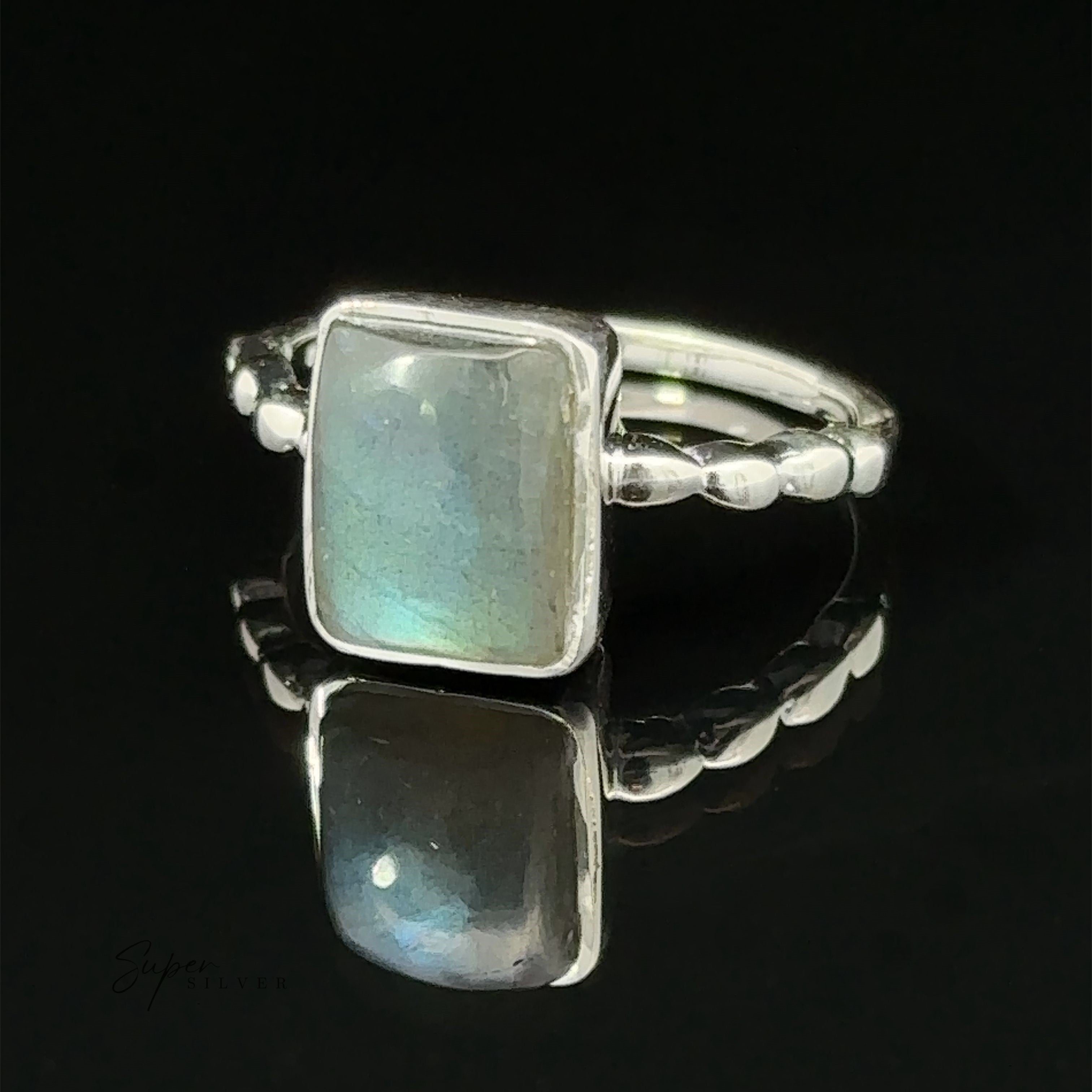 A Rectangle Gemstone Ring with Beaded Band with a rectangular moonstone set on top, displayed on a reflective black surface.