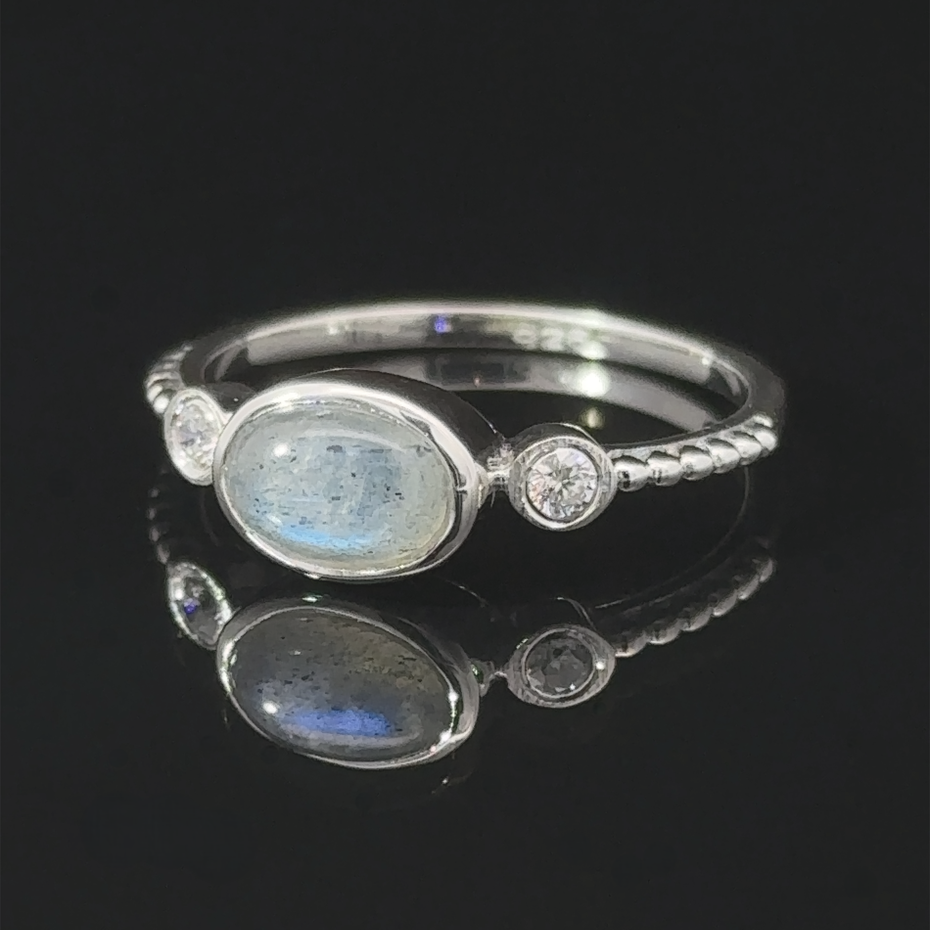 Handcrafted Horizontal Oval Gemstone Ring with Beaded Band and two small diamonds, displayed on a reflective black surface.