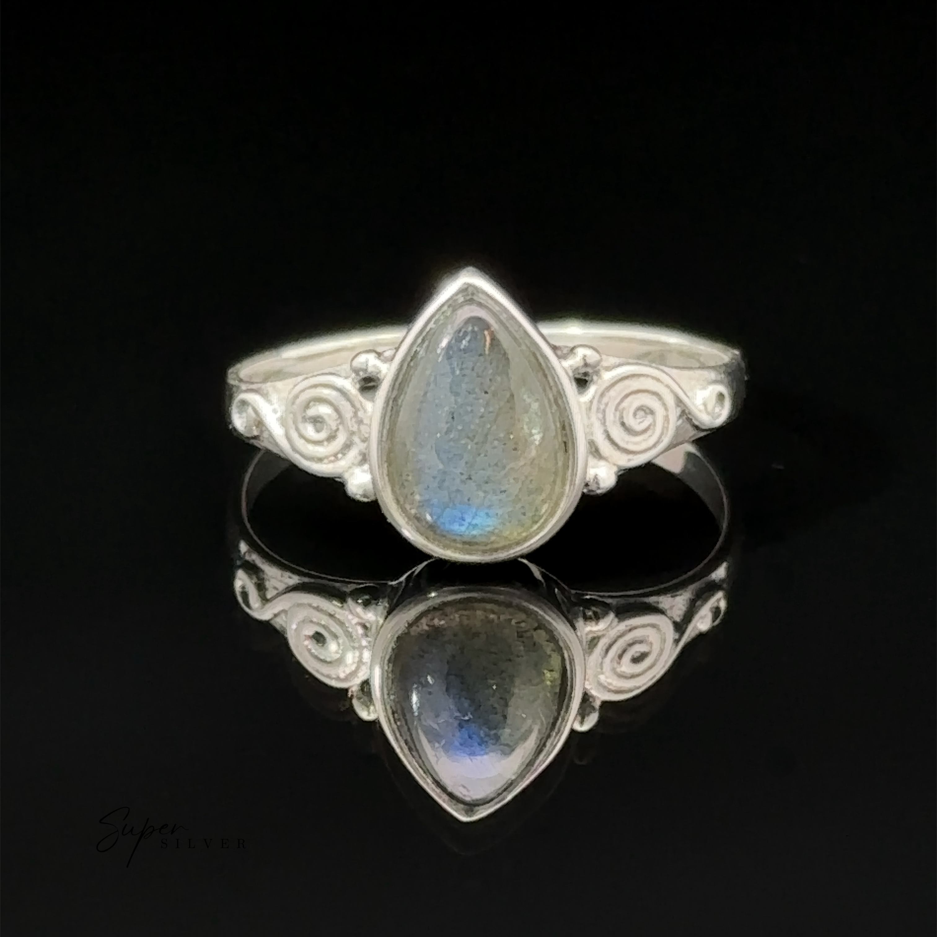 A teardrop gemstone ring with swirls, displayed on a reflective black surface with the logo "sajensilver" in the corner.