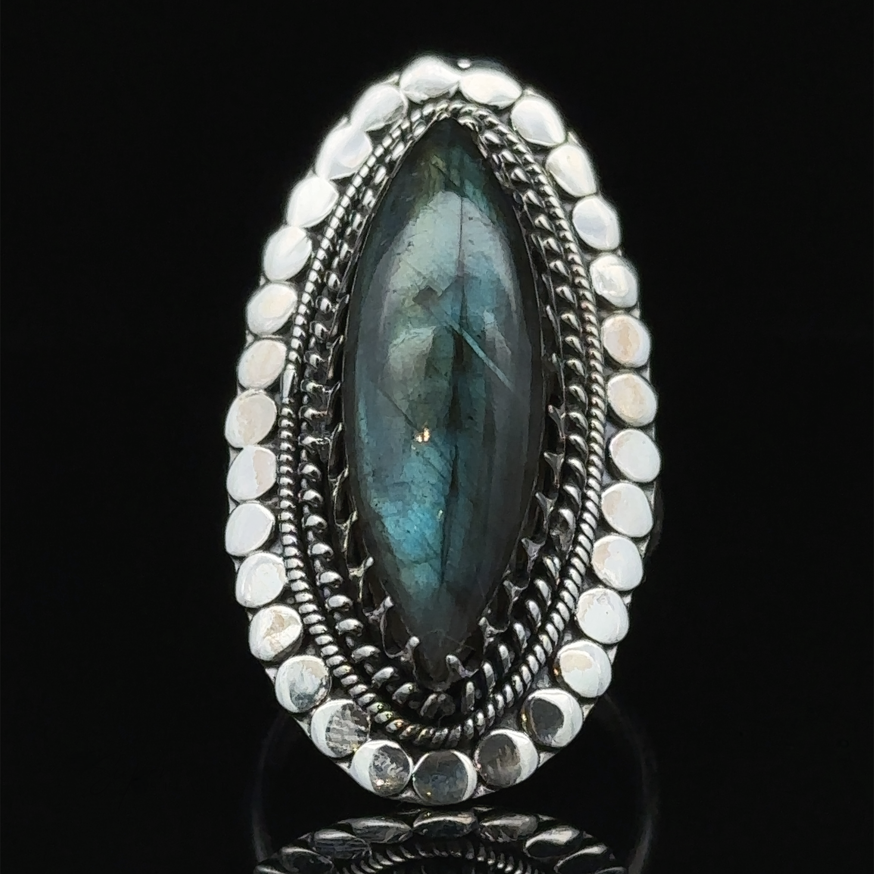 A Statement Marquise Shaped Gemstone Ring with a large, oval-shaped blue-green gemstone, surrounded by intricate detailing and small silver beads, embodies the essence of bohemian jewelry. Set against a black background, this piece is truly eye-catching.