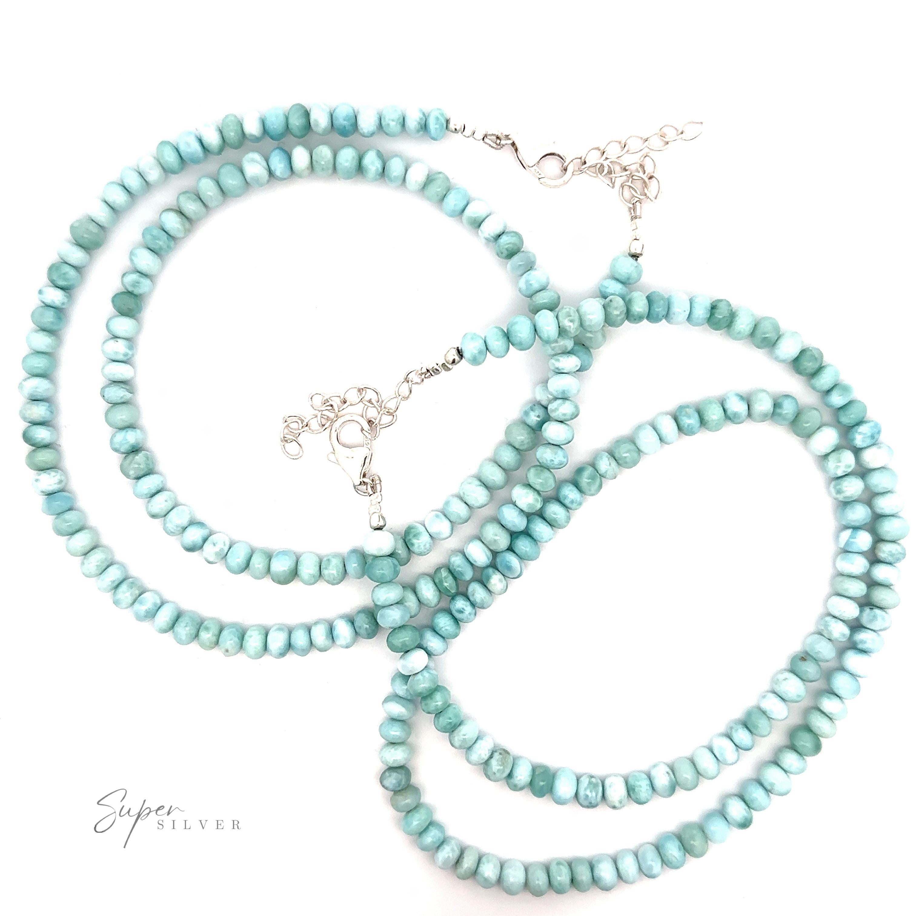 A turquoise beaded necklace with small, round beads and silver clasps arranged in loops against a white background, reminiscent of a Larimar Beaded Necklace.