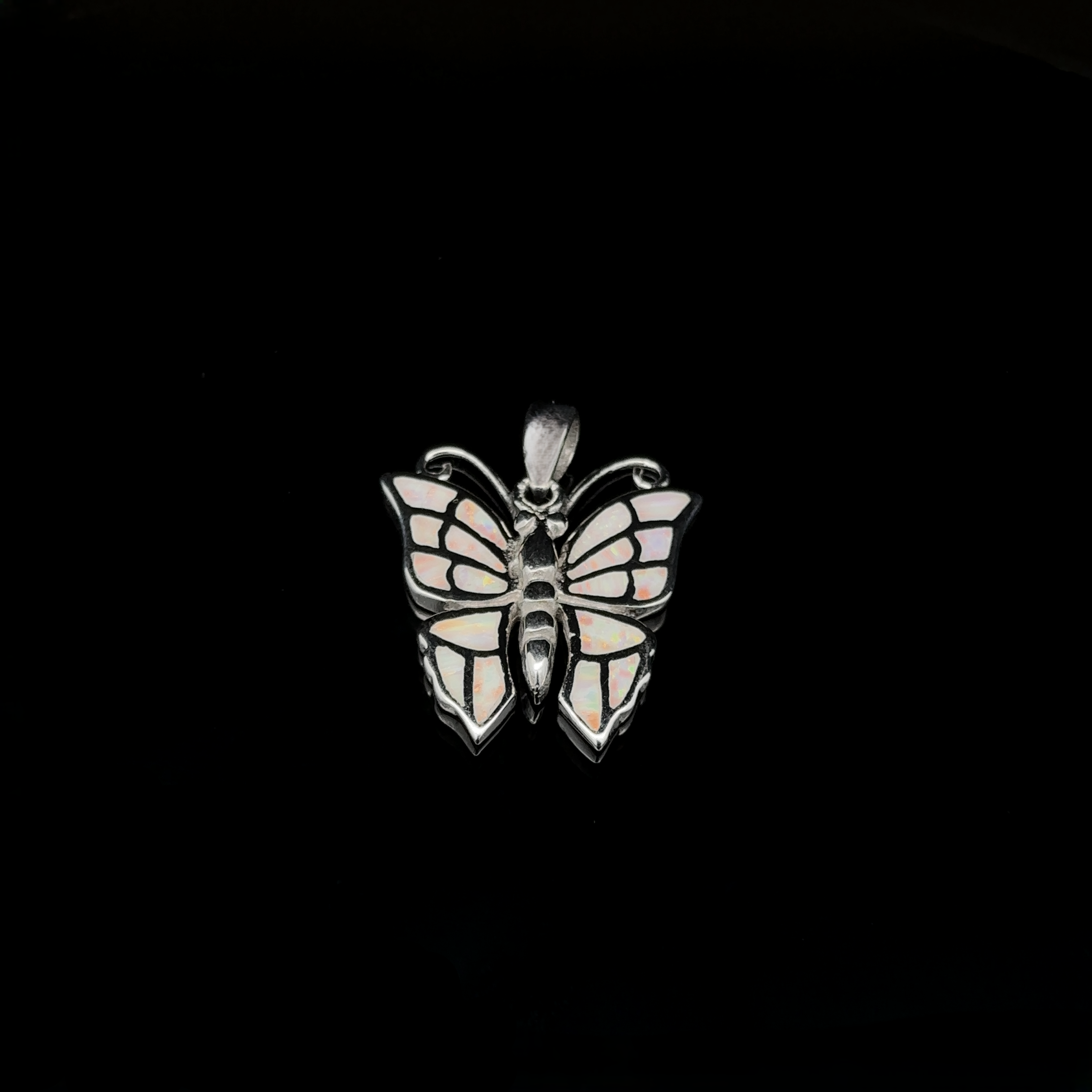 The Lab-Created Opal Butterfly Pendant features a stunning sterling silver design with wings resembling stained glass, set against a black background.