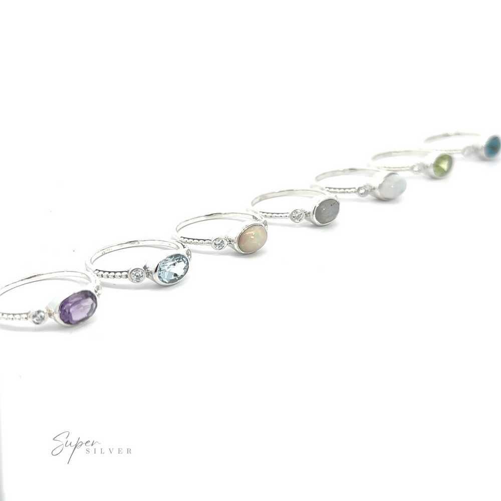 
                  
                    Several Horizontal Oval Gemstone Rings with Beaded Bands displayed in a row on a white background.
                  
                