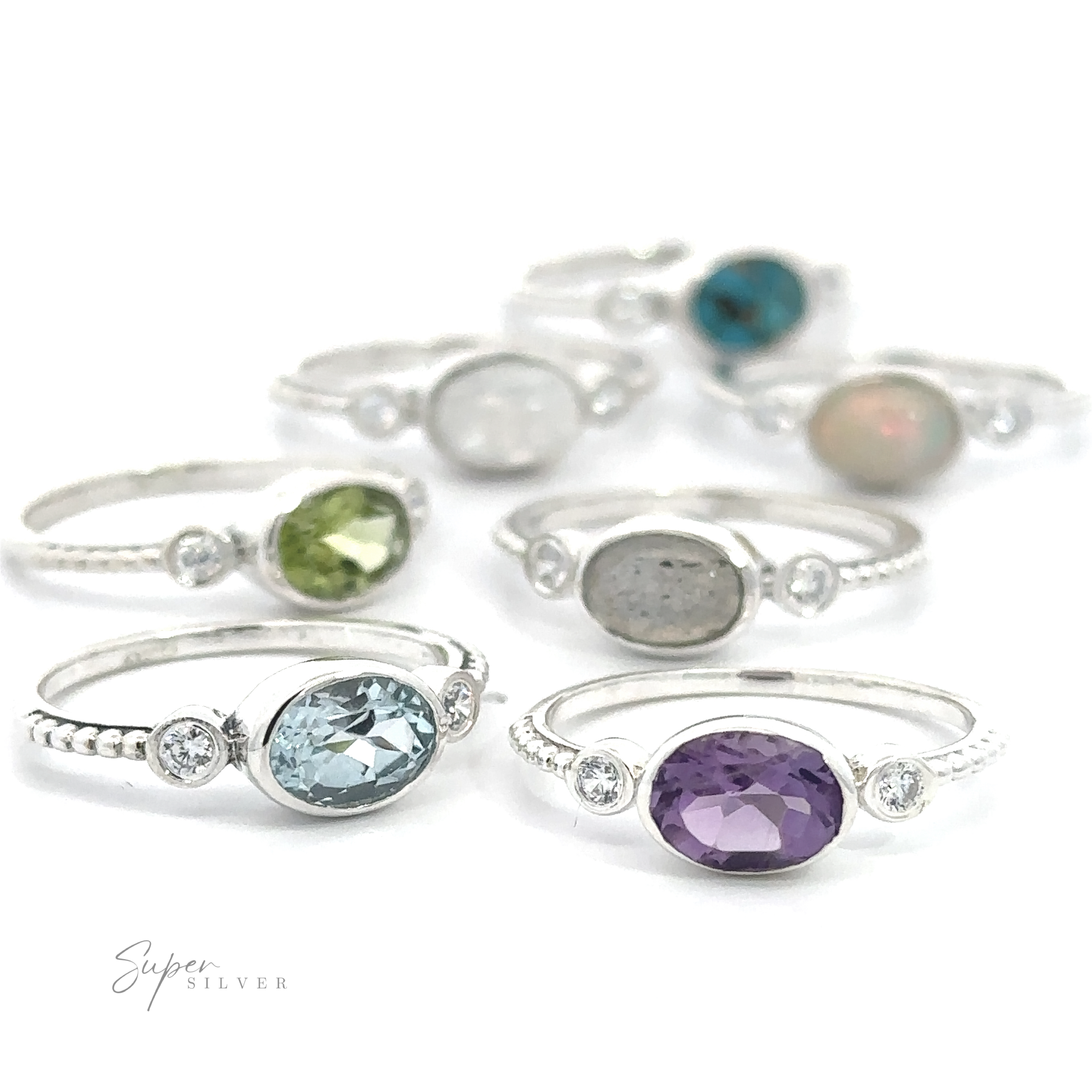 A collection of Horizontal Oval Gemstone Rings with Beaded Bands displayed on a white surface, featuring different stones and designs, with a logo branded at the bottom right.