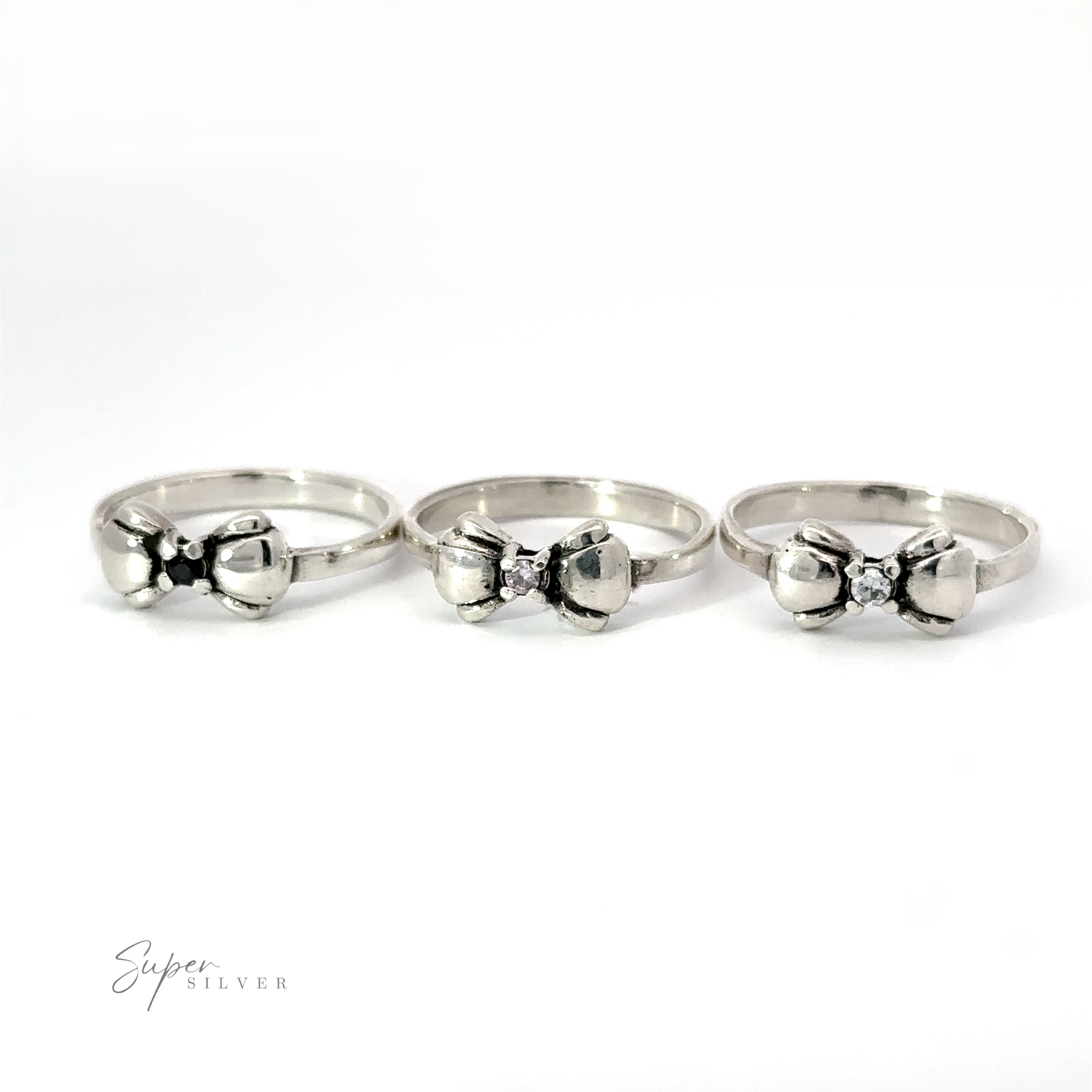 Three Adorable Cubic Zirconia Bow Rings with bow-shaped designs and small central gemstones are lined up against a white background. One features a striking black cubic zirconia. The text "Super Silver" is visible in the lower left corner.