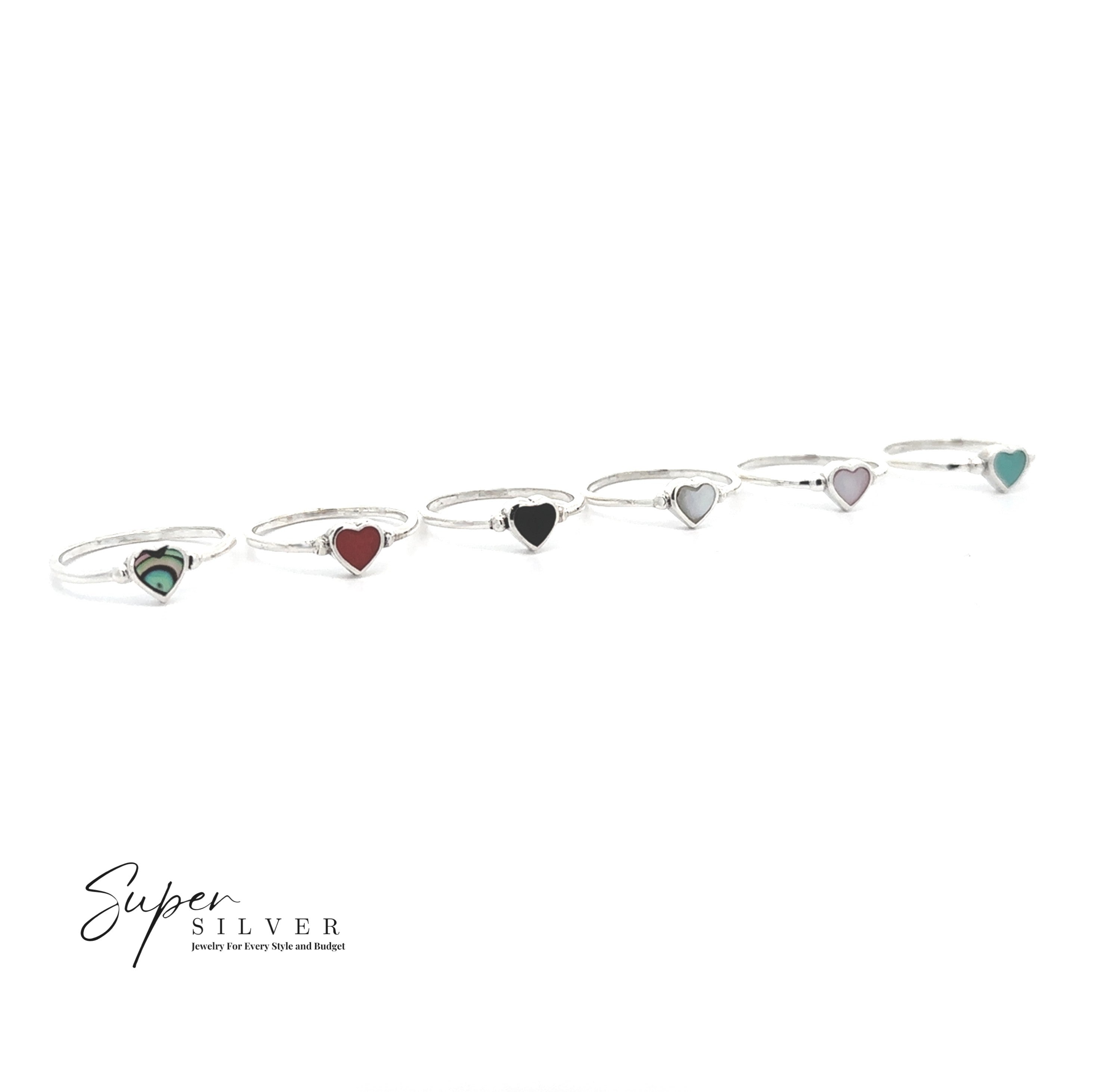 Six Dainty Inlaid Heart Rings, each with a colorful heart-shaped stone and sterling silver band, are lined up on a white background. The "Super Silver" logo is visible in the lower left corner.